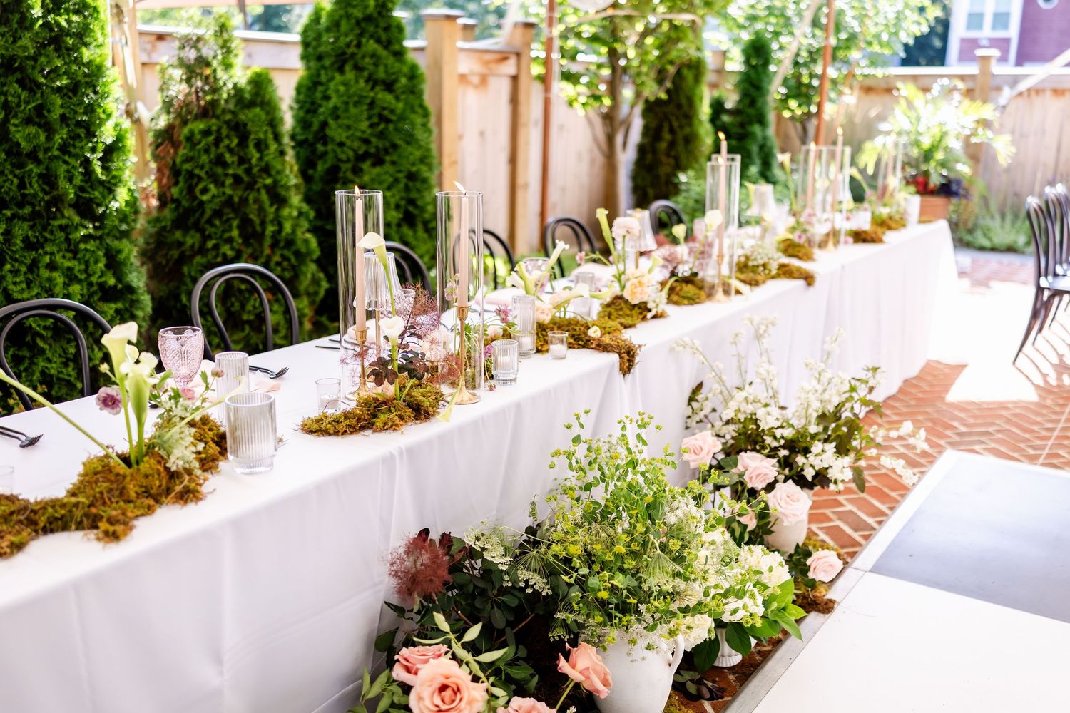 Elegant wedding reception tables decorated with white linens and floral centerpieces in an outdoor setting.