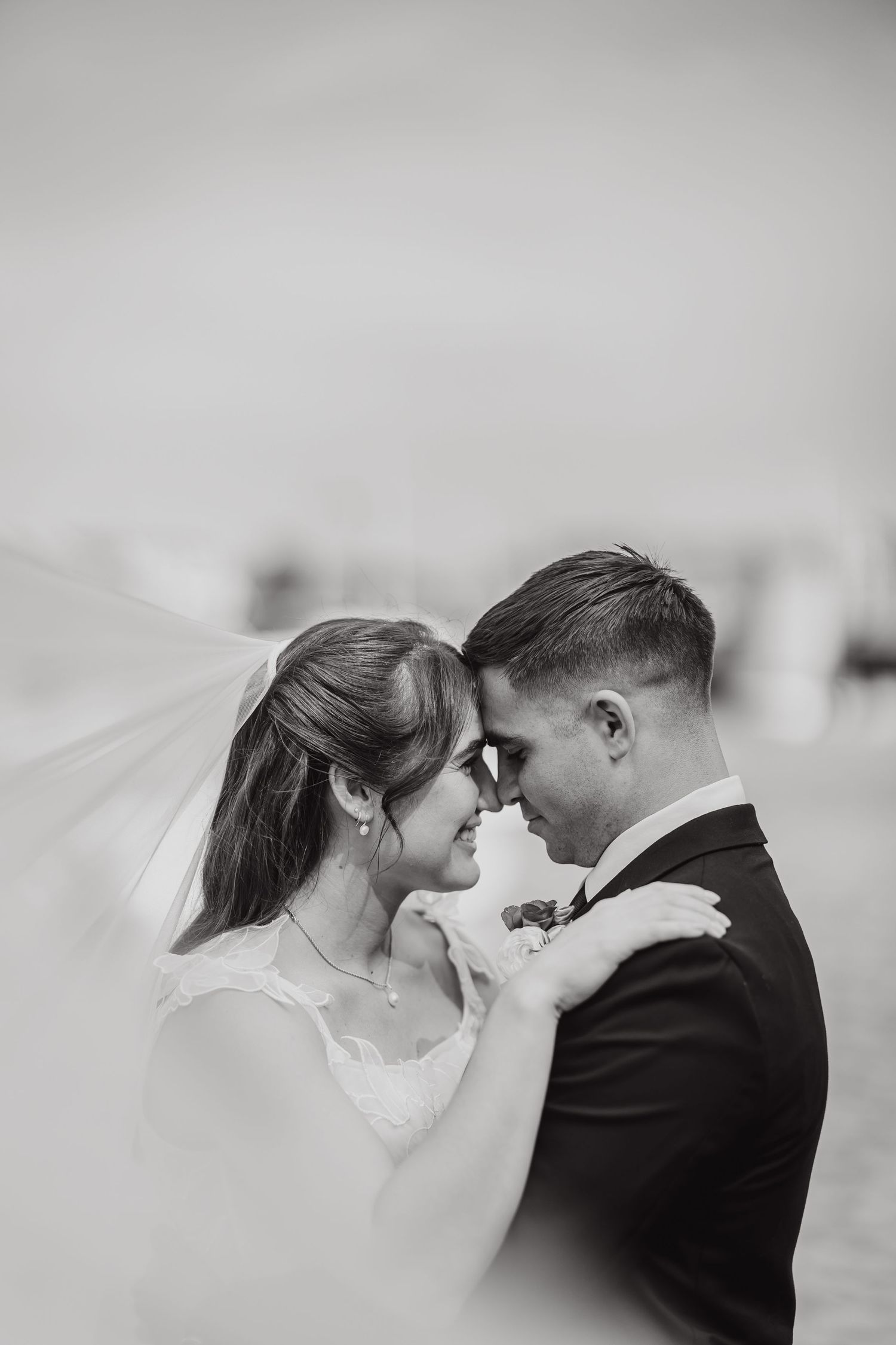 Romantic black and white close-up of newlyweds sharing an intimate moment with bride's veil flowing.