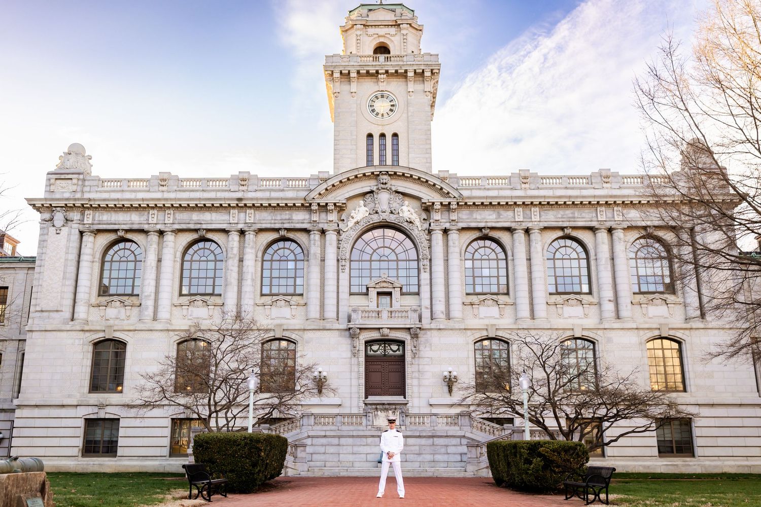 Person in white outfit standing before a grand neoclassical building with clock tower on a university campus.