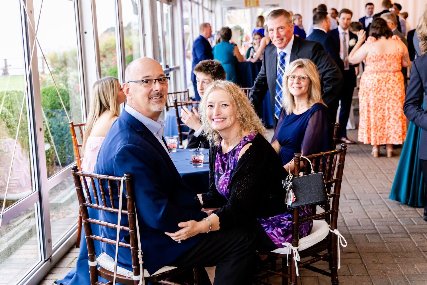 Wedding reception guests enjoying conversation in a bright windowed venue.
