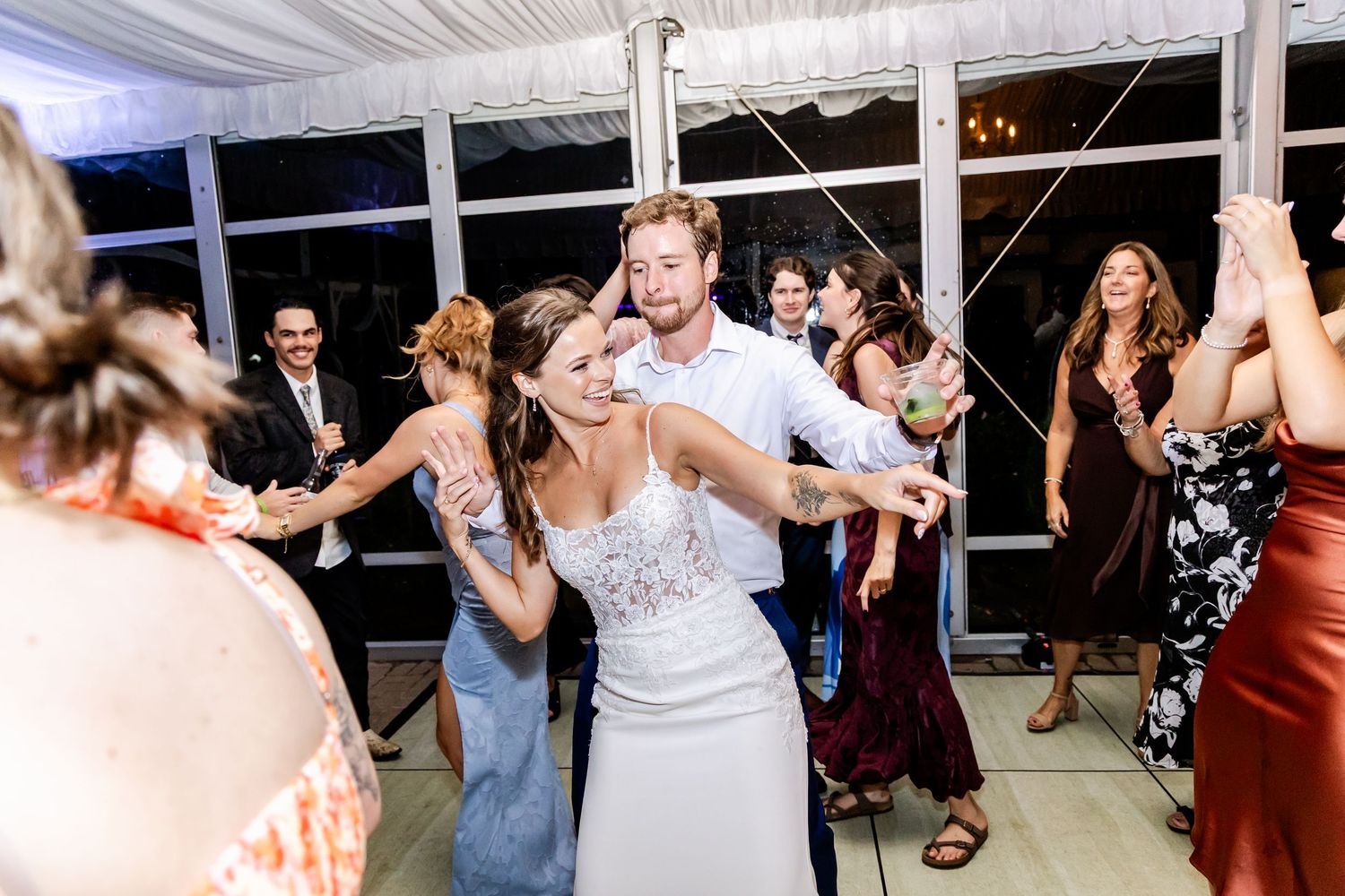 Wedding party dancing energetically on a tented dance floor during evening reception festivities.