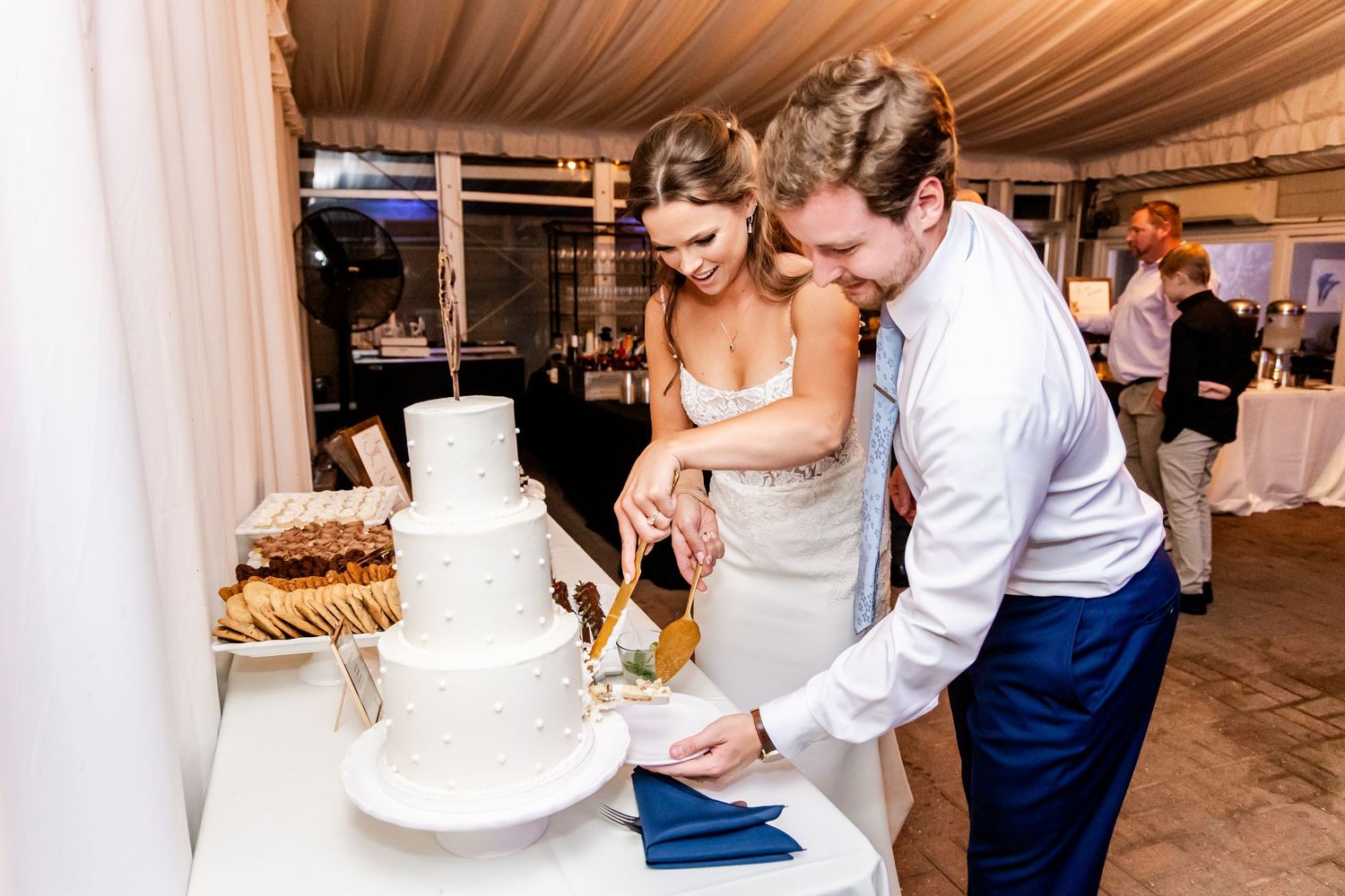 Wedding celebration featuring a traditional white tiered cake cutting moment at an indoor reception.