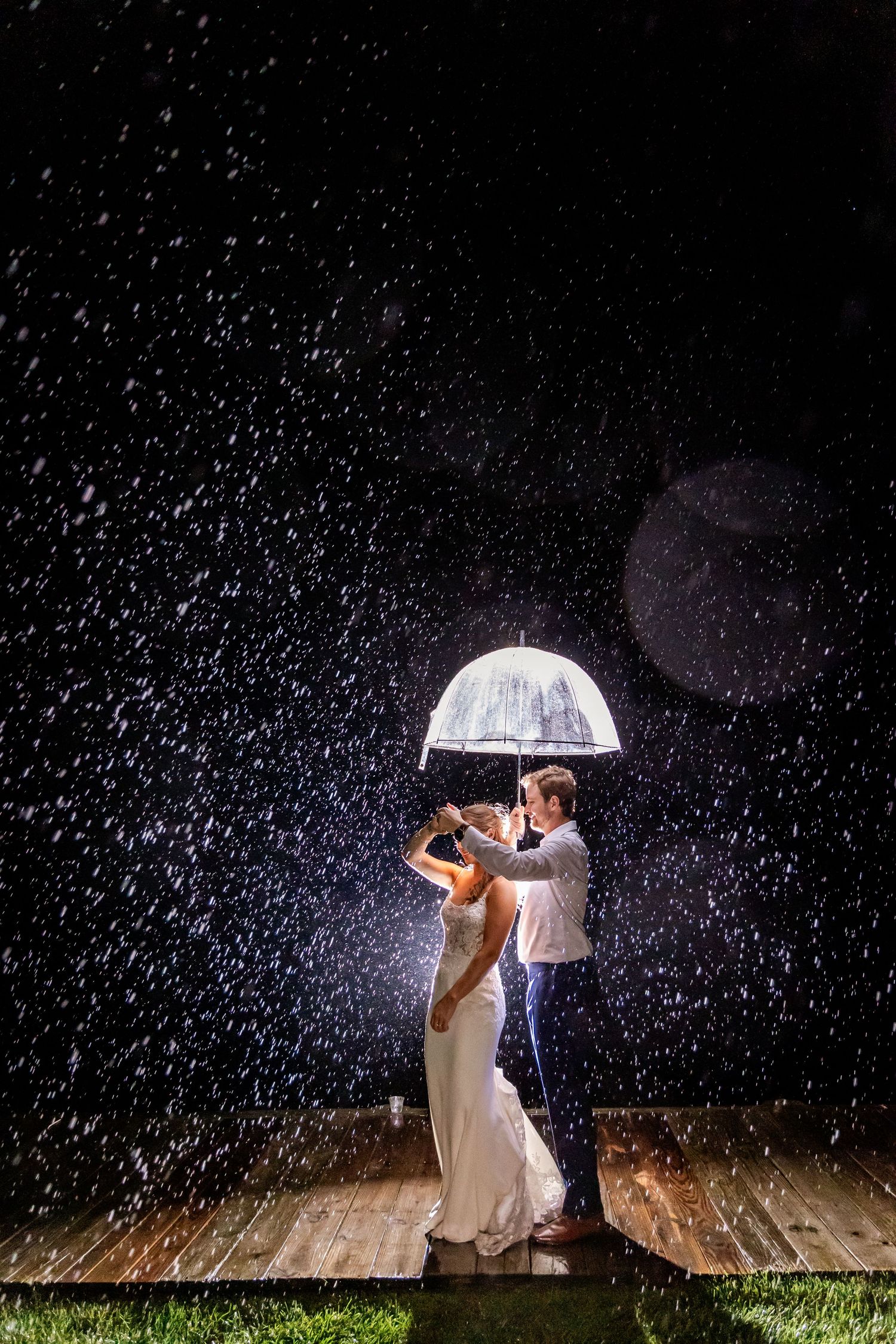 A couple shares an intimate moment under a clear umbrella as rain falls dramatically around them.