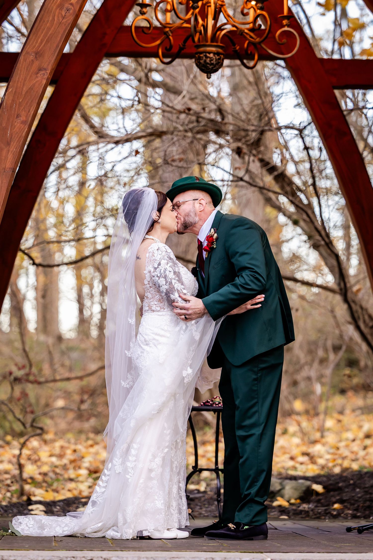A romantic moment under a wooden arch decorated with an elegant chandelier in an autumn forest setting.