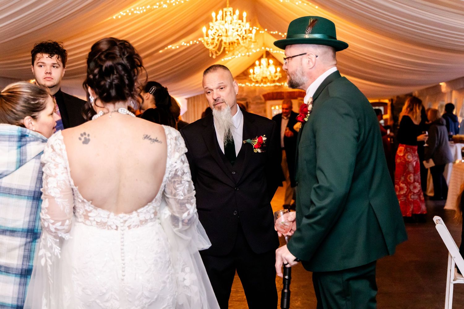 Wedding celebration inside an elegant tent with chandeliers as people gather on the dance floor during a reception.
