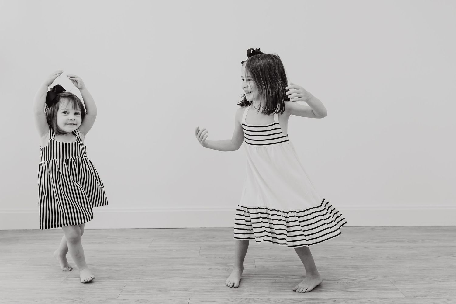 Two children in striped dresses dance and twirl together in a playful black and white photograph.