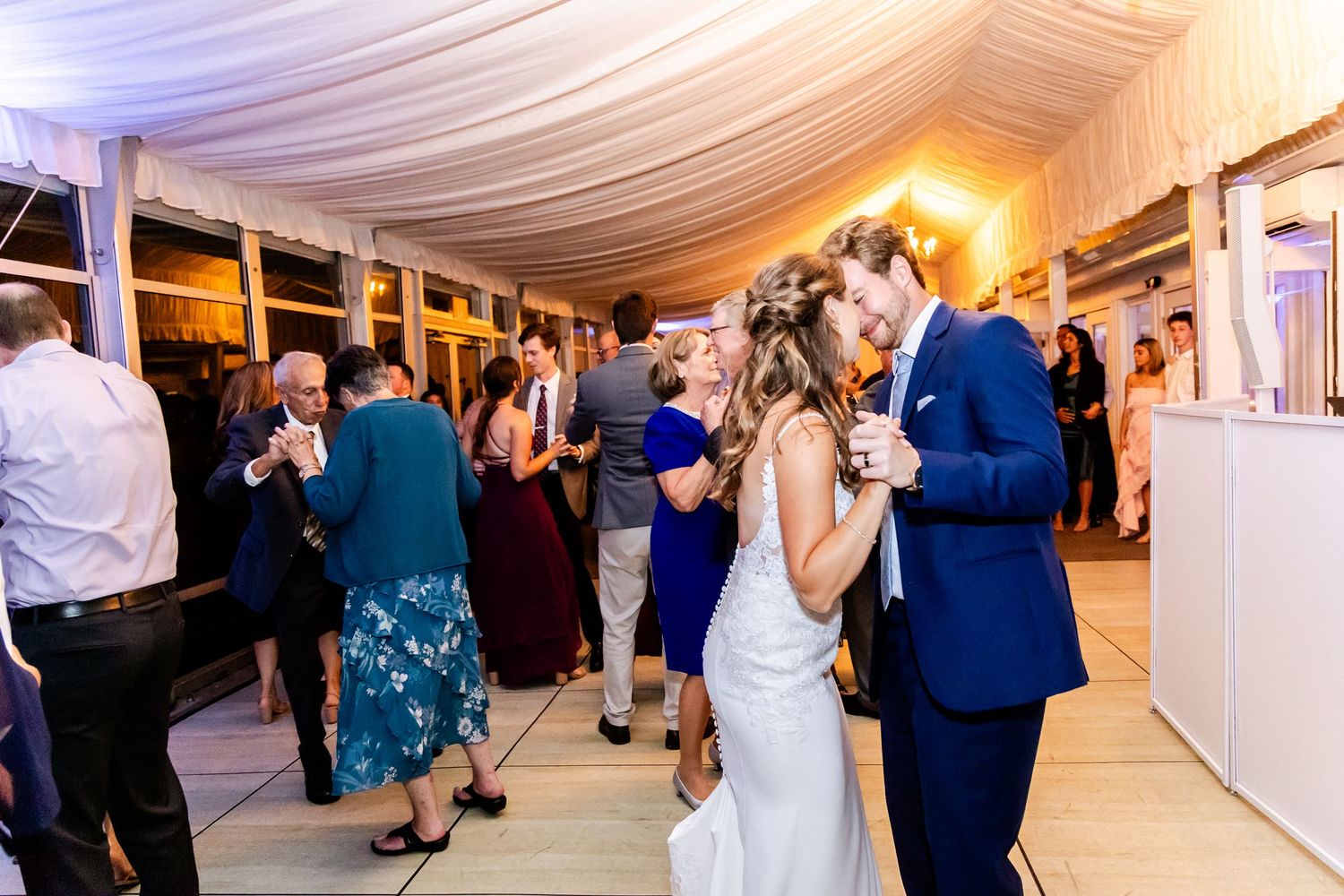 Wedding celebration in an elegant white tent with fabric draped ceiling and ambient lighting.