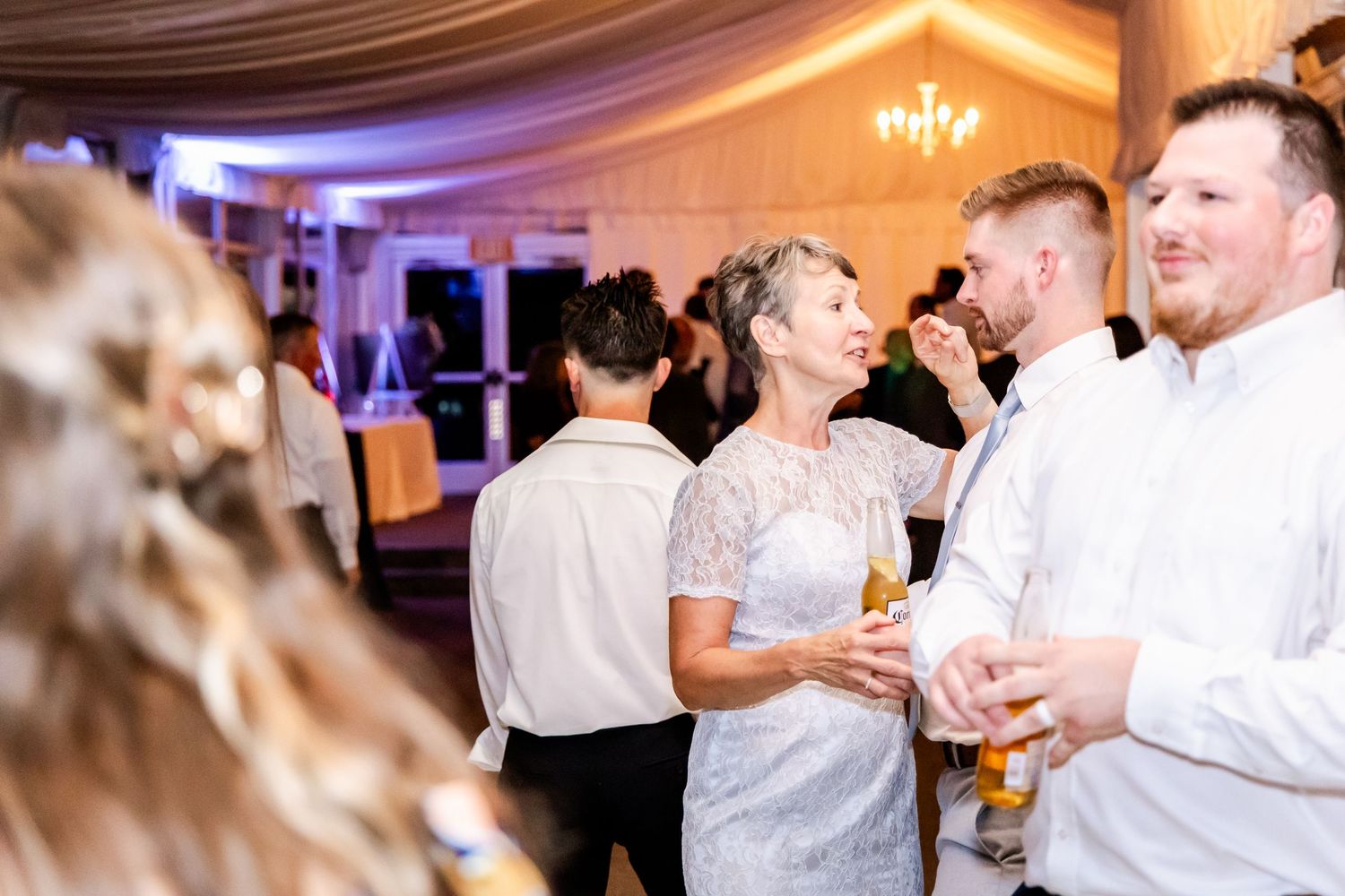 Wedding guests dancing and mingling during reception under warm lighting and draped ceiling.