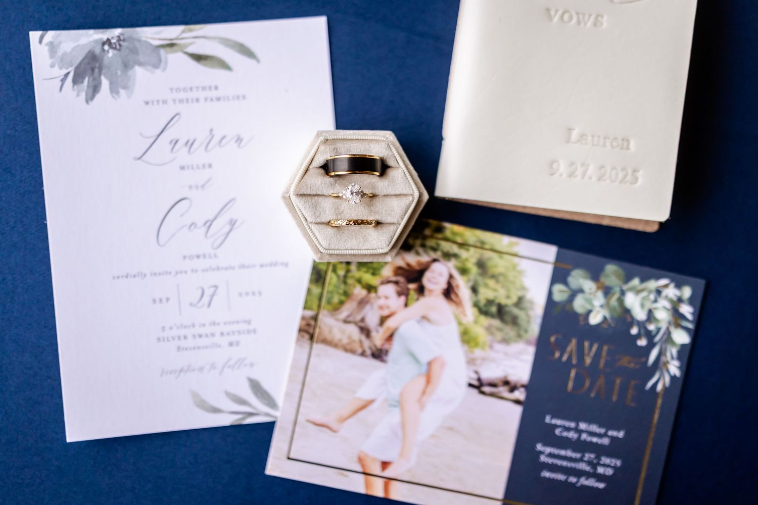 Wedding invitations and stationery with floral designs laid out on a navy blue background.
