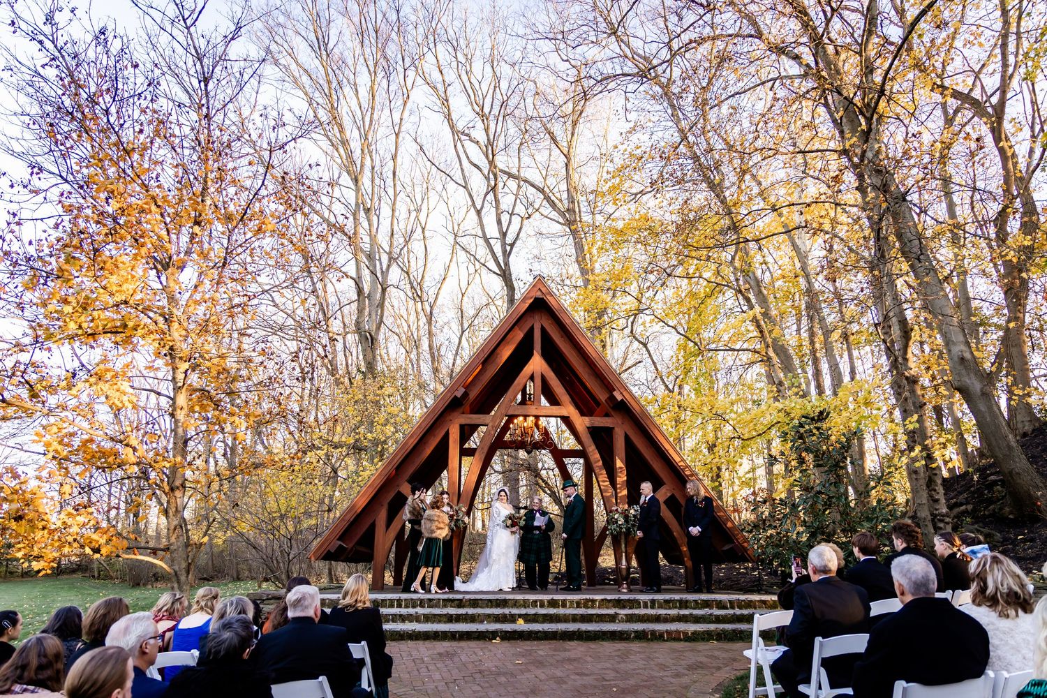 Wooden outdoor wedding pavilion surrounded by fall foliage and trees.