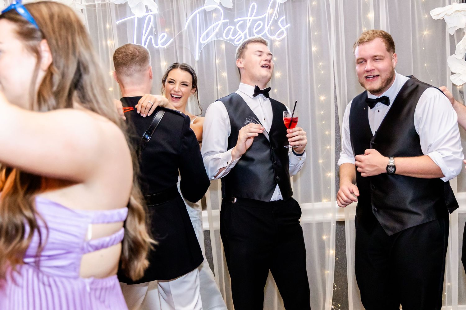 Wedding party dancing and celebrating in front of a decorated white backdrop.