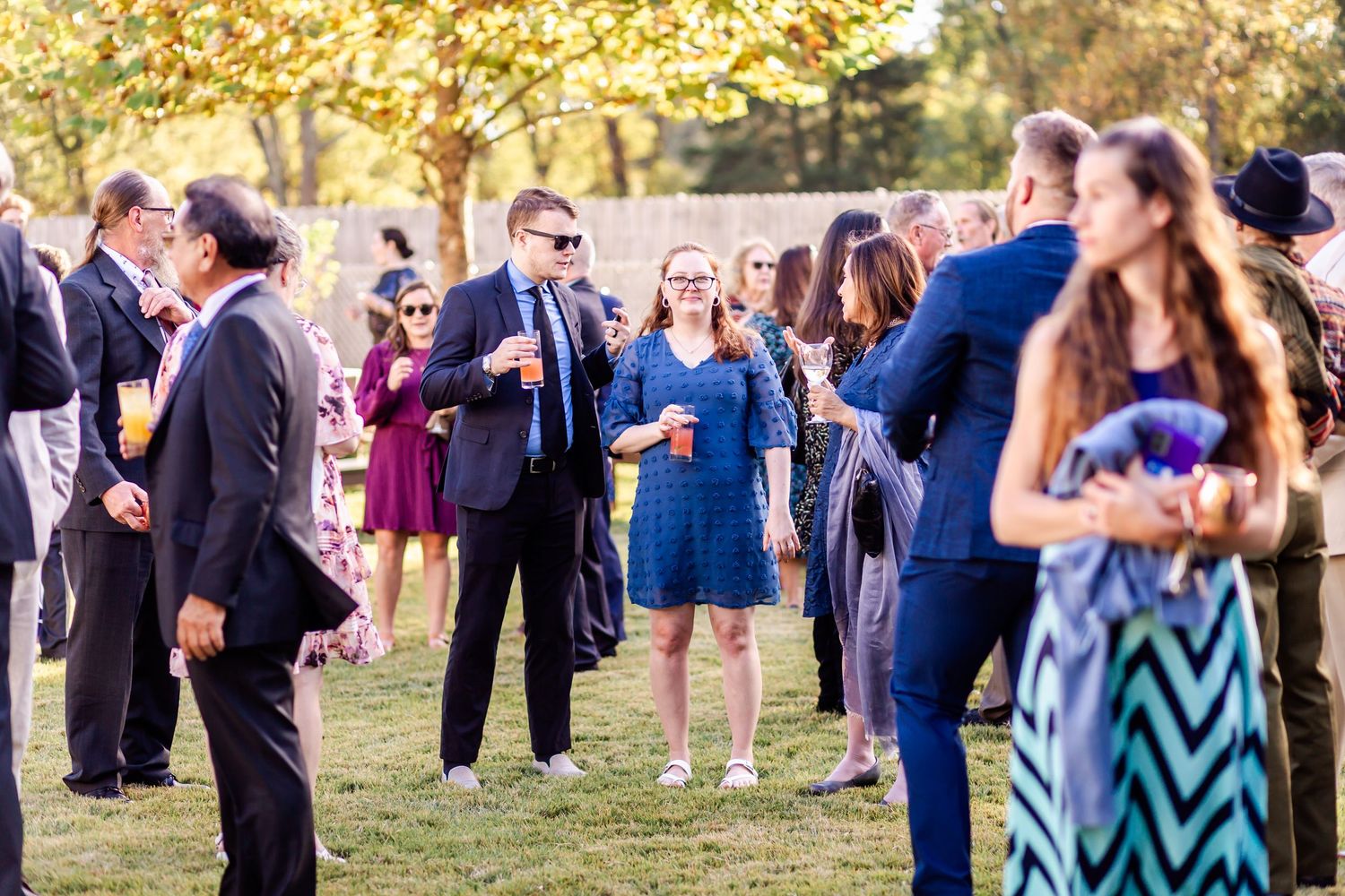 Wedding guests mingle and socialize at an outdoor reception during golden hour.