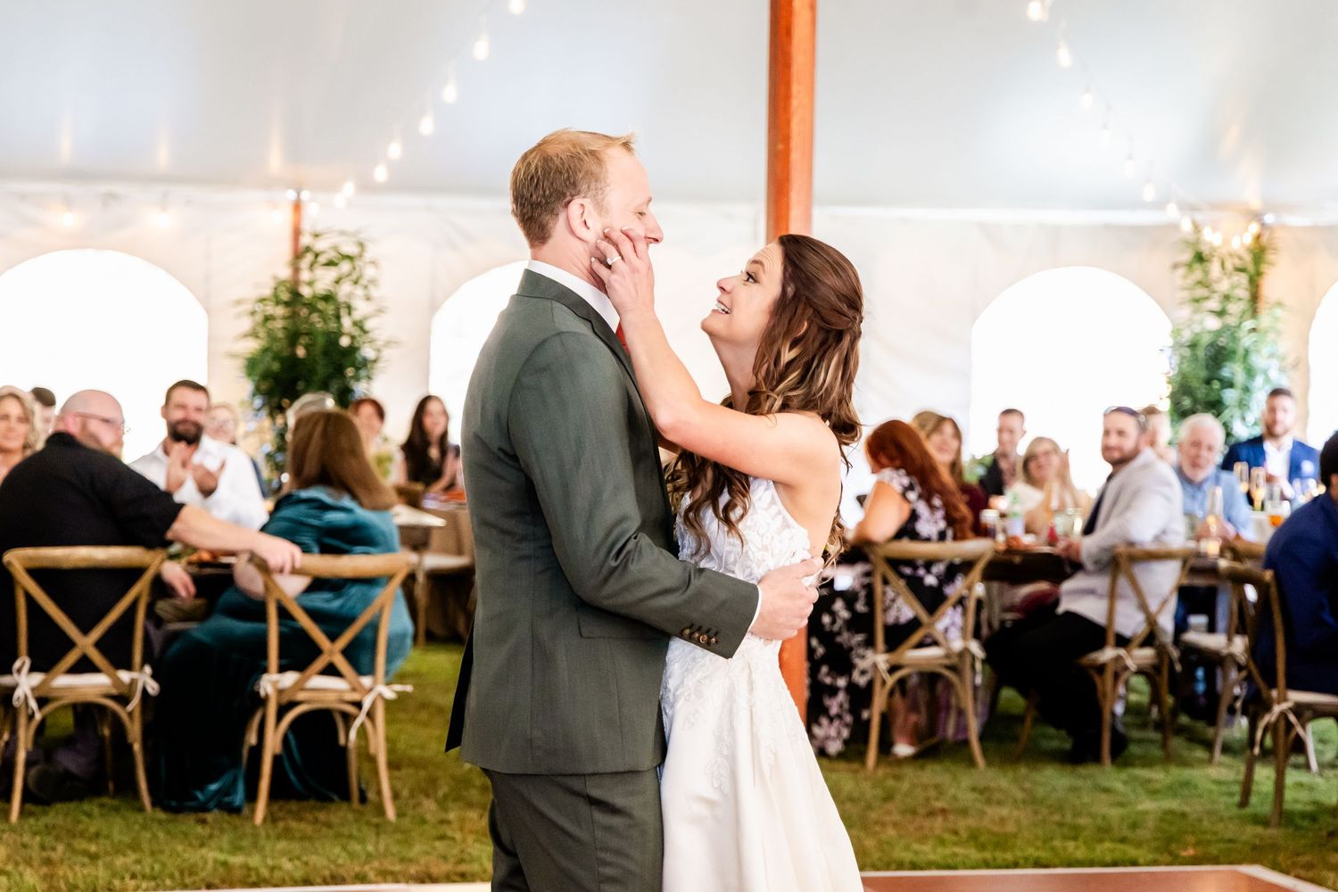 Wedding reception celebration under a white tent with string lights and wooden cross-back chairs.