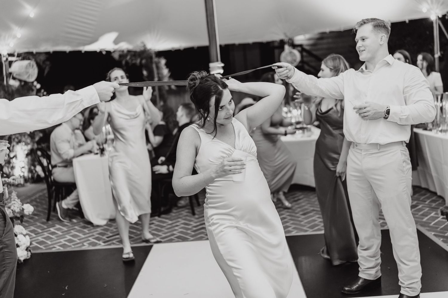 Wedding guests dance energetically in black and white under a tent at an outdoor reception.