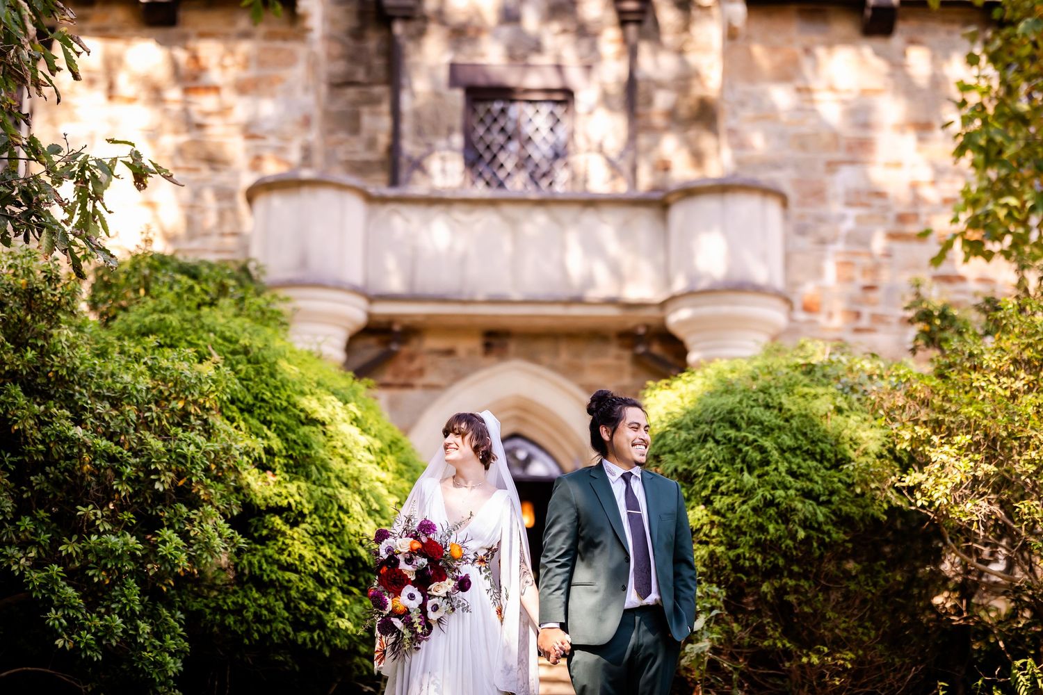 Wedding party poses for photos outside a historic stone building.