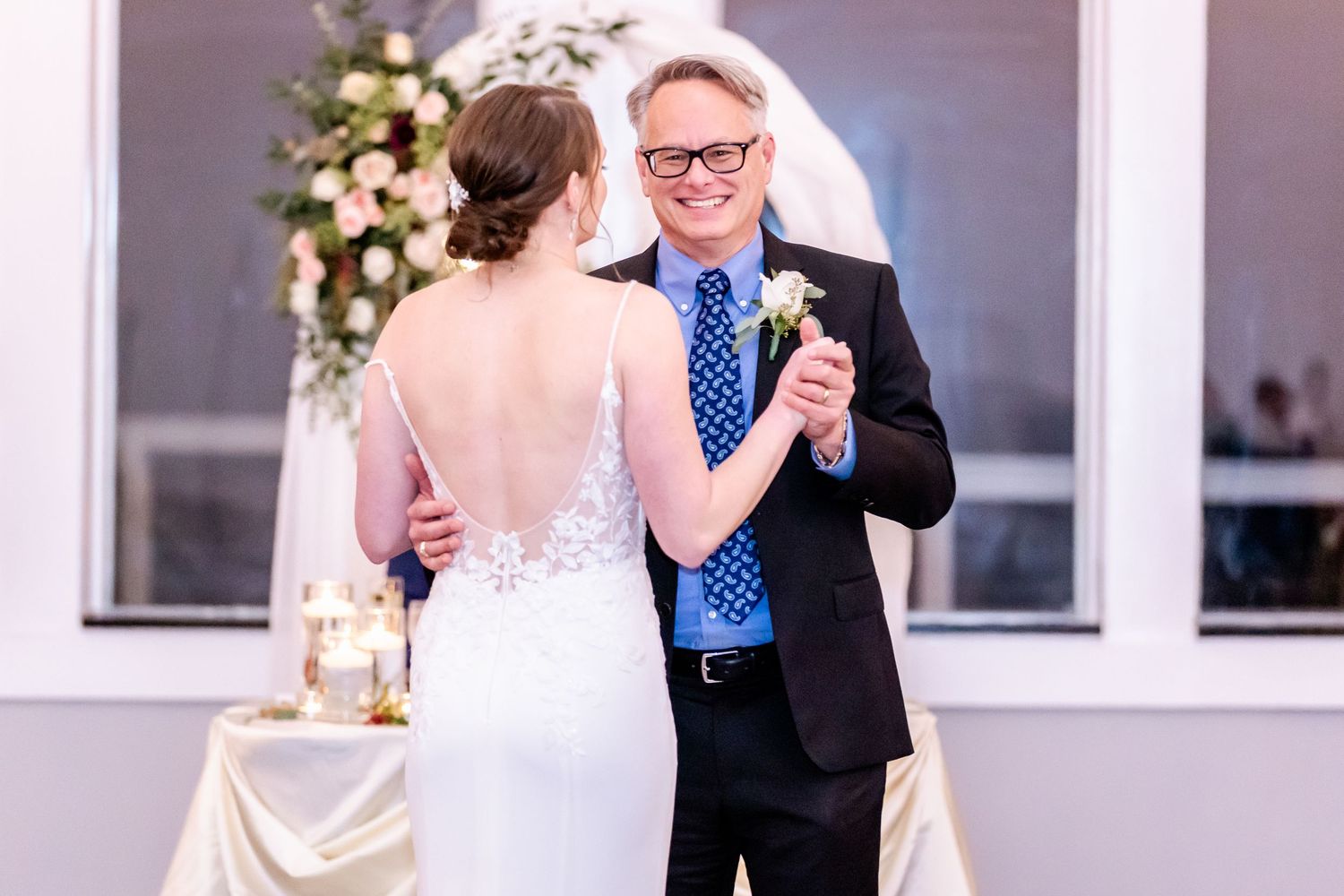 Two people share a joyful moment during a wedding reception with floral decorations and table settings in the background.