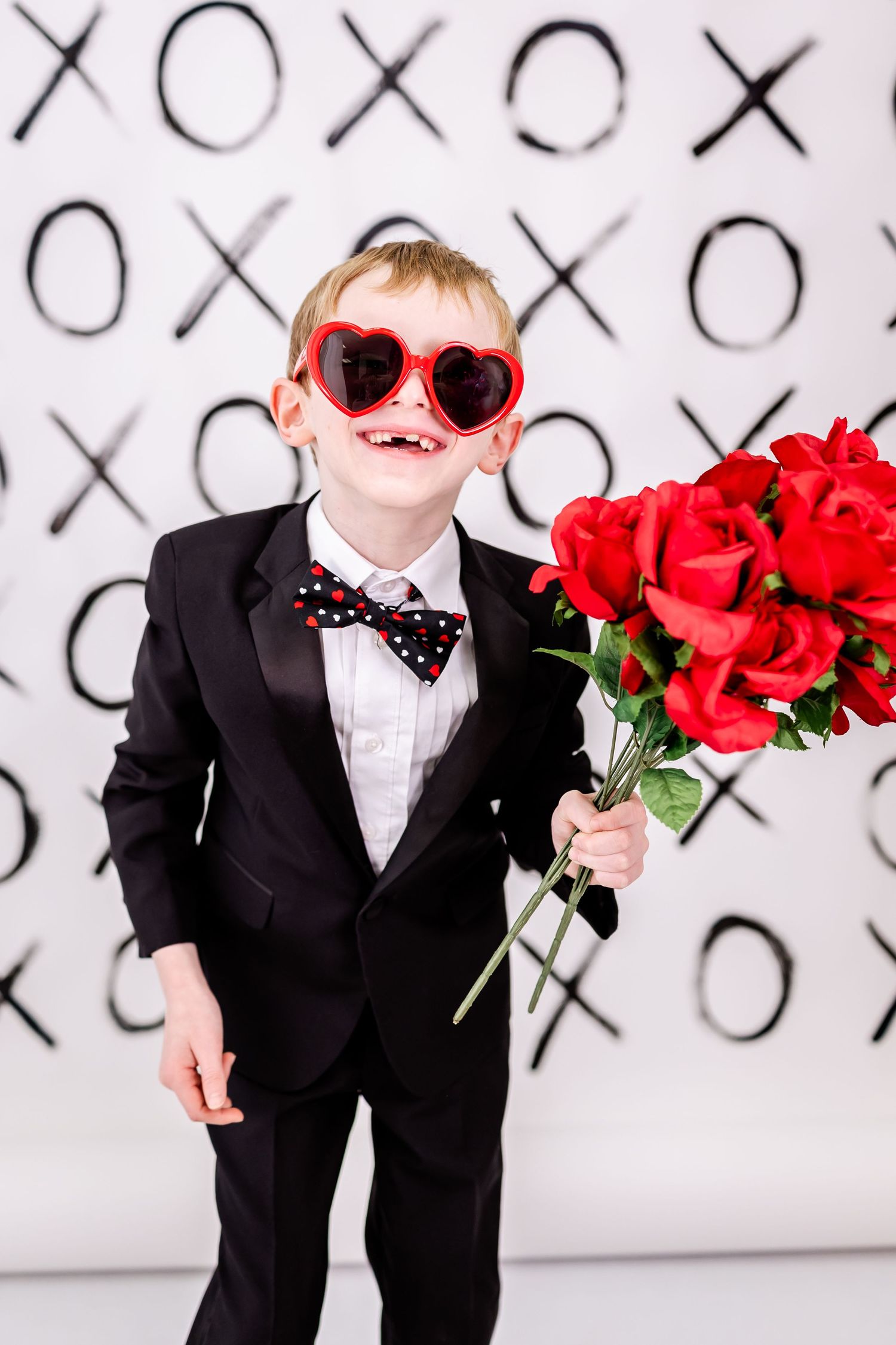 Dapper black suit and red heart sunglasses with Valentine roses against X's and O's backdrop.