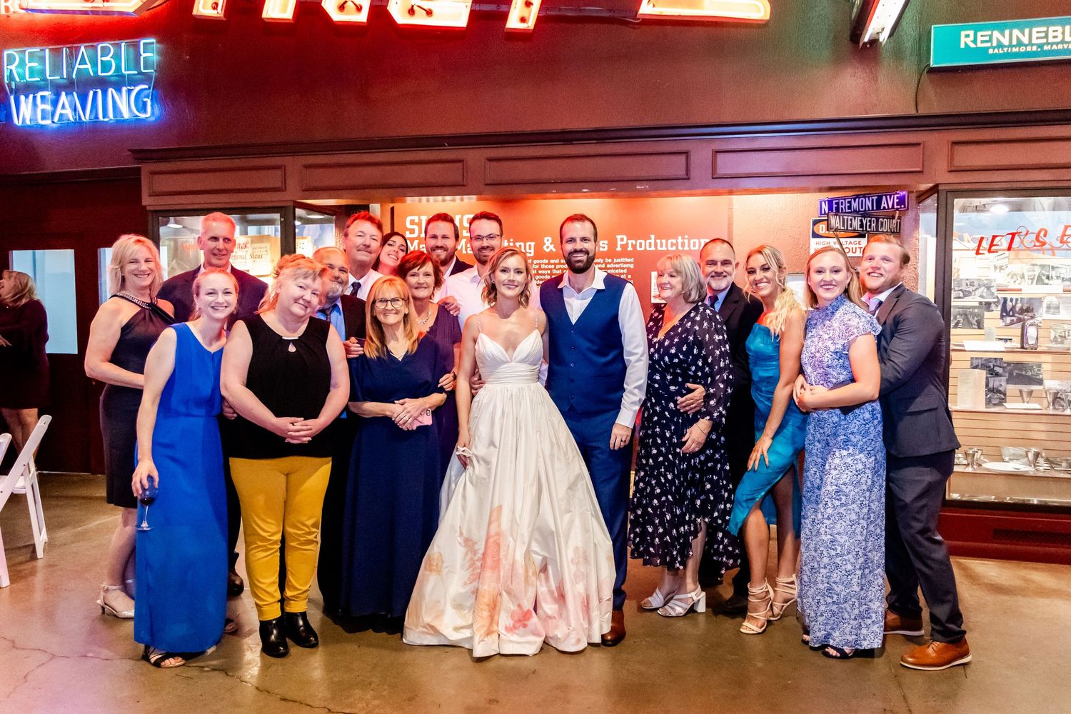 Large wedding party group photo with bride in pink dress at indoor venue.