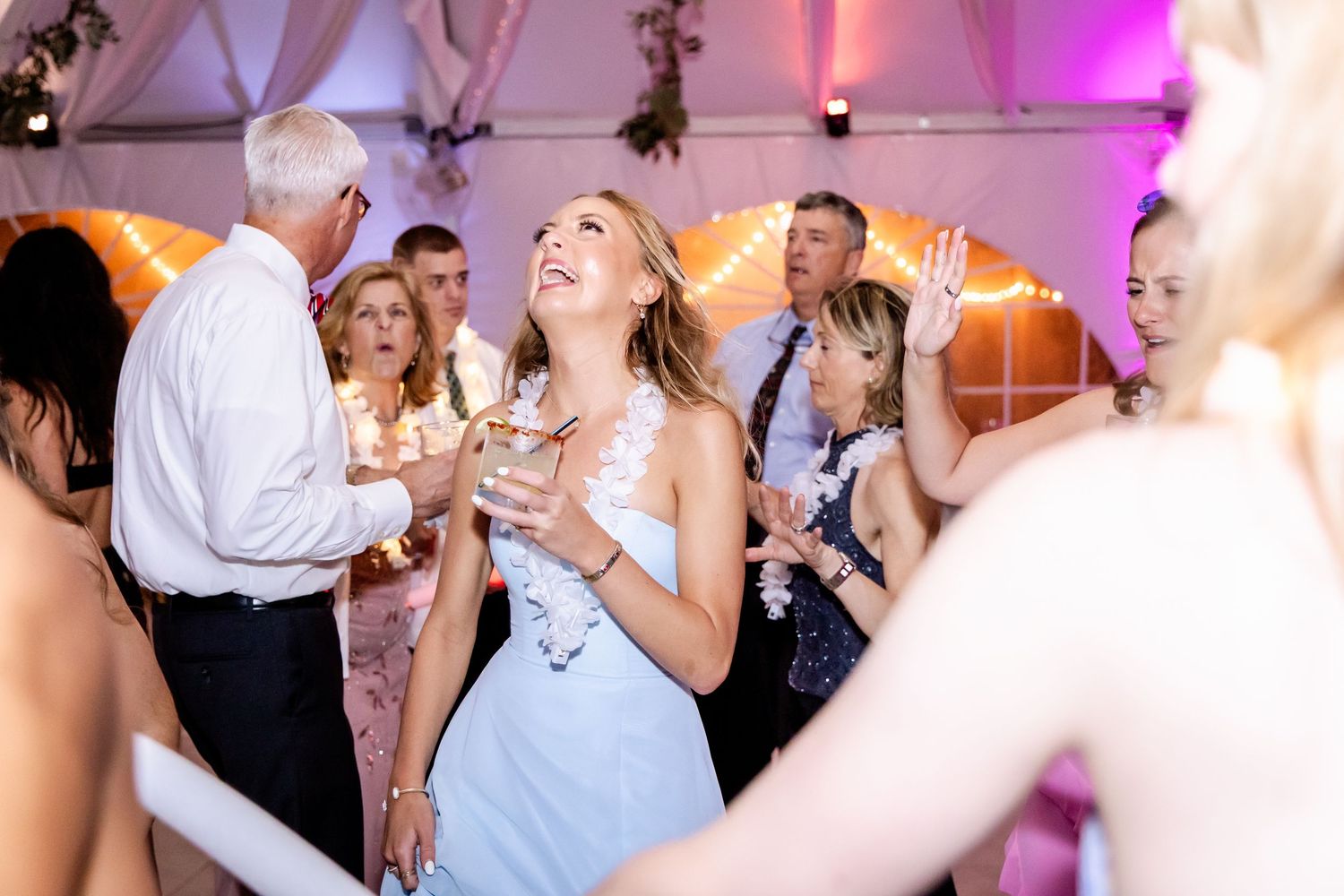 Wedding reception dance floor filled with guests celebrating under pink lighting.