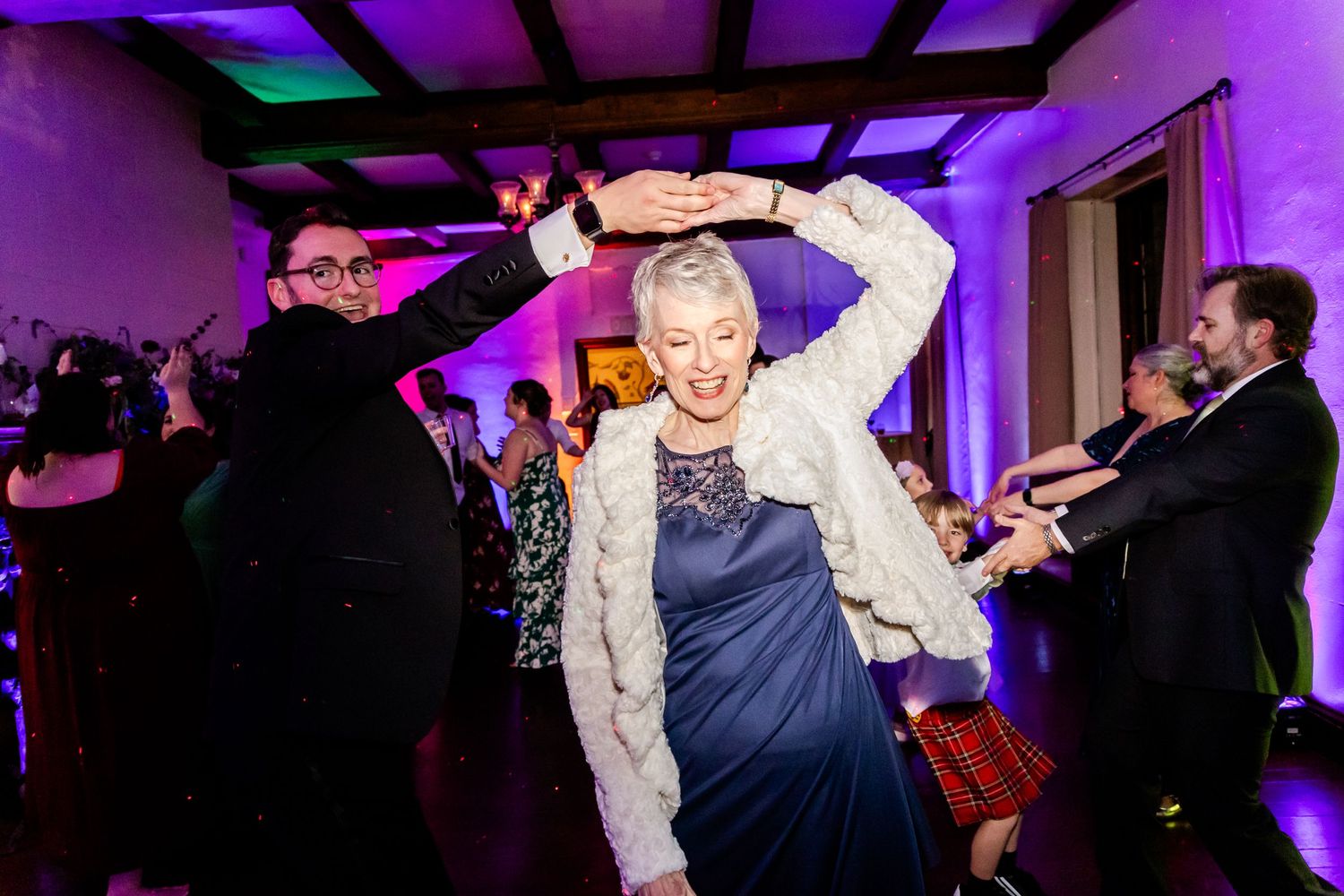 Wedding reception dance party with purple lighting and people dancing enthusiastically.
