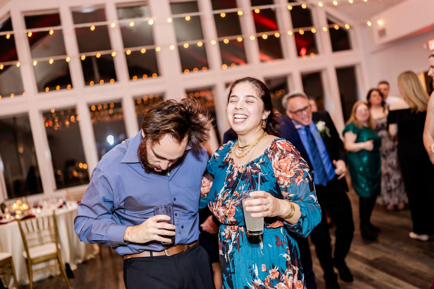Wedding guests enjoying drinks and conversation under twinkling string lights at an indoor reception.