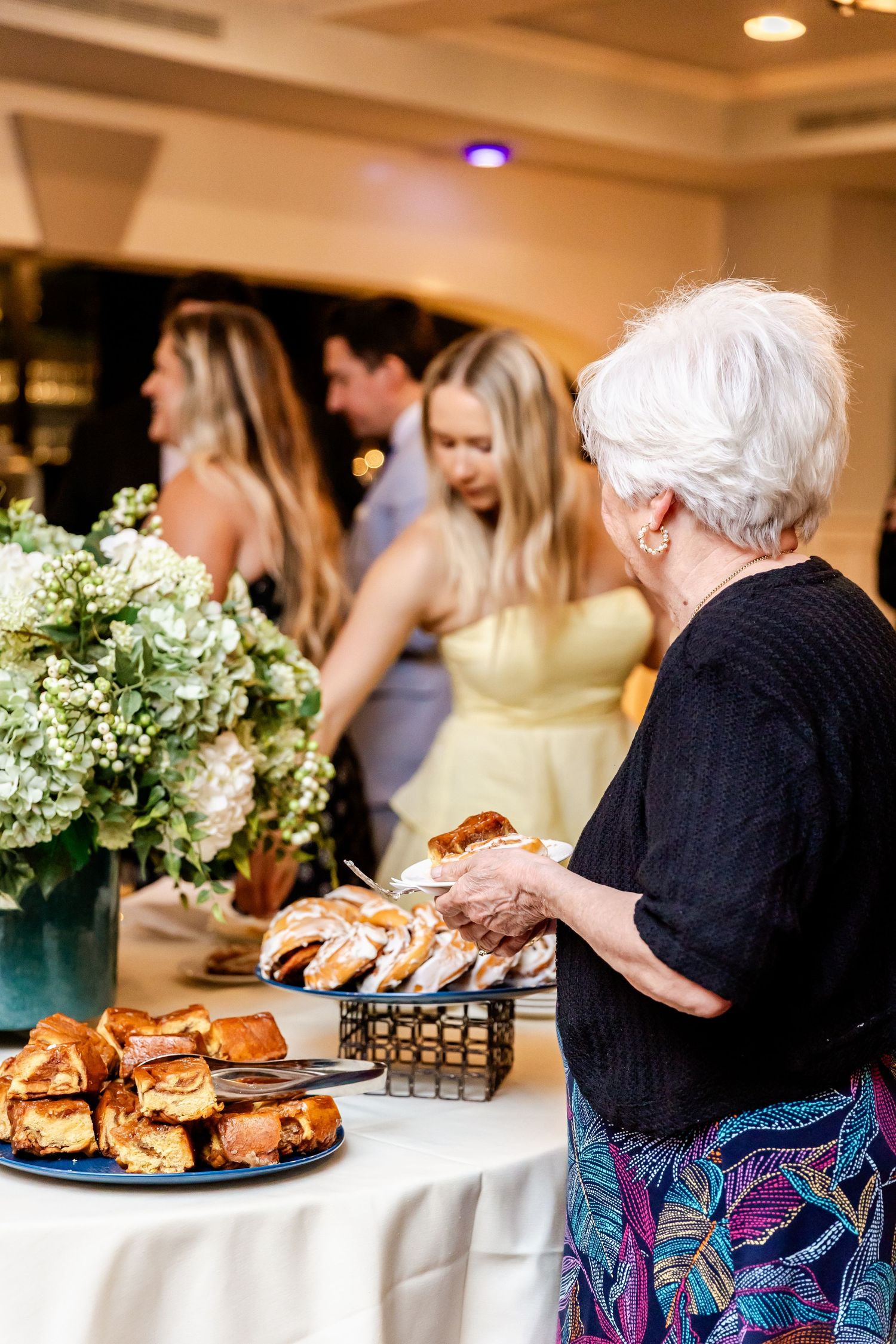Reception buffet table with pastries and floral centerpieces being prepared for wedding guests.