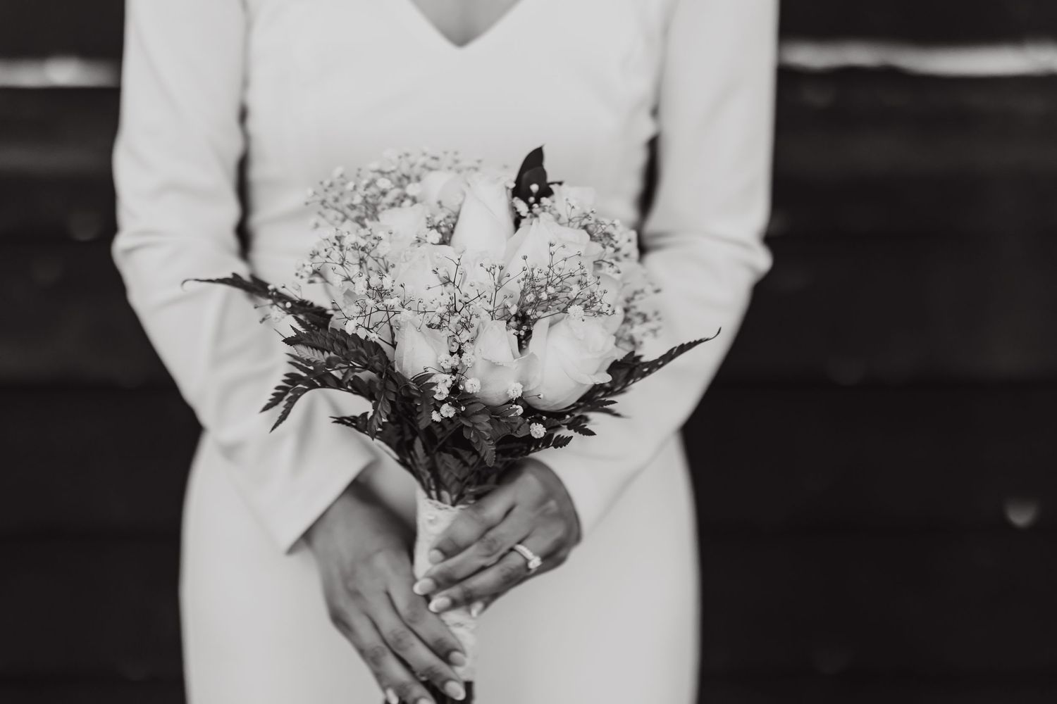 Close-up of hands holding an elegant white and green wedding bouquet against a white dress.