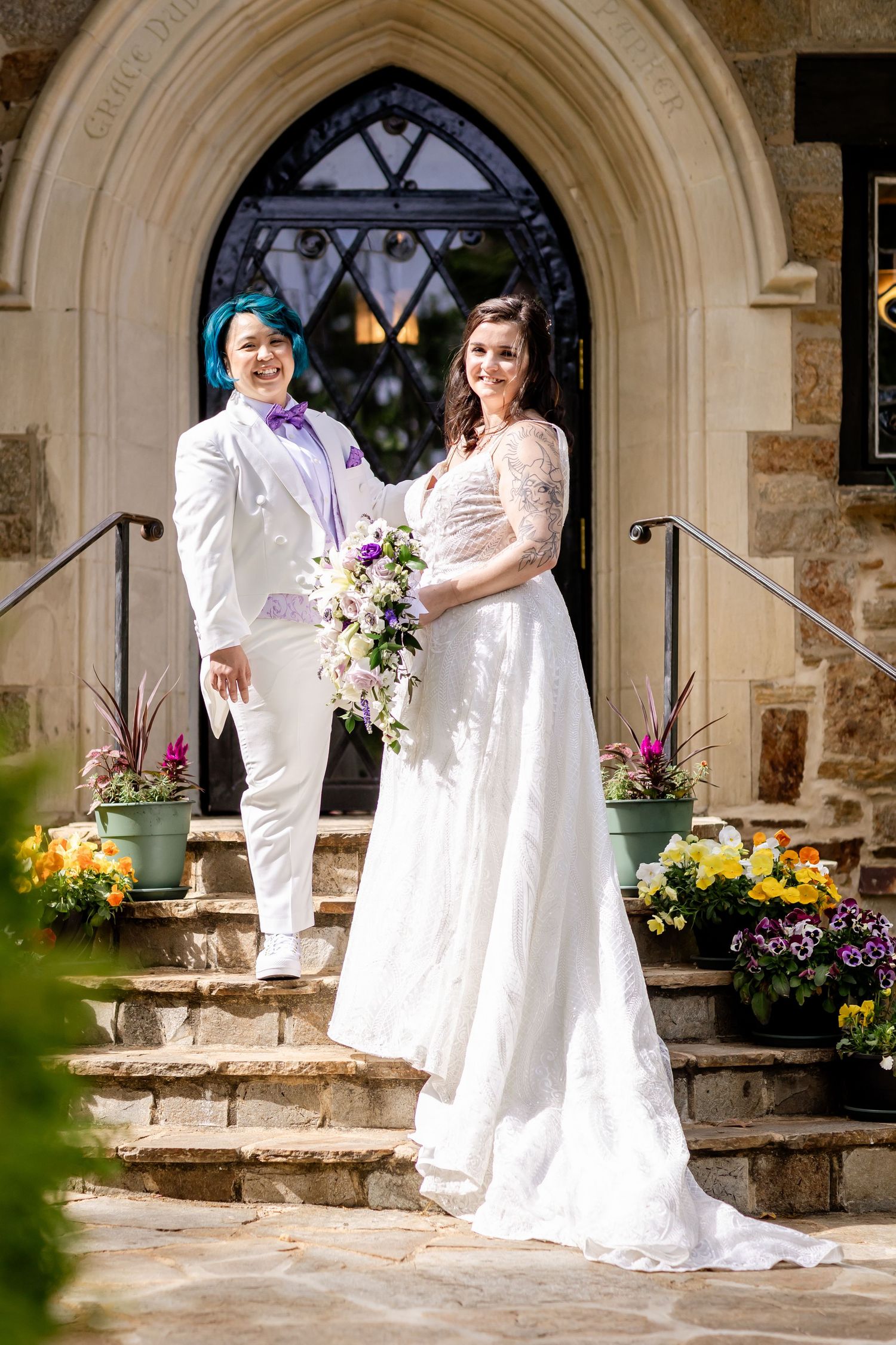 Couple in wedding attire pose on church steps decorated with colorful flowers.