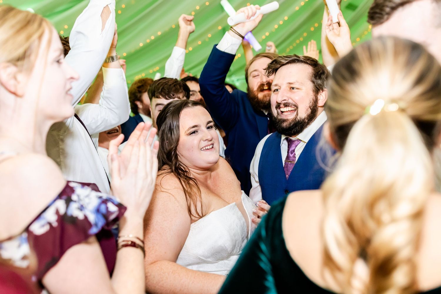 Wedding guests dance and celebrate with enthusiasm under elegant draped lighting.