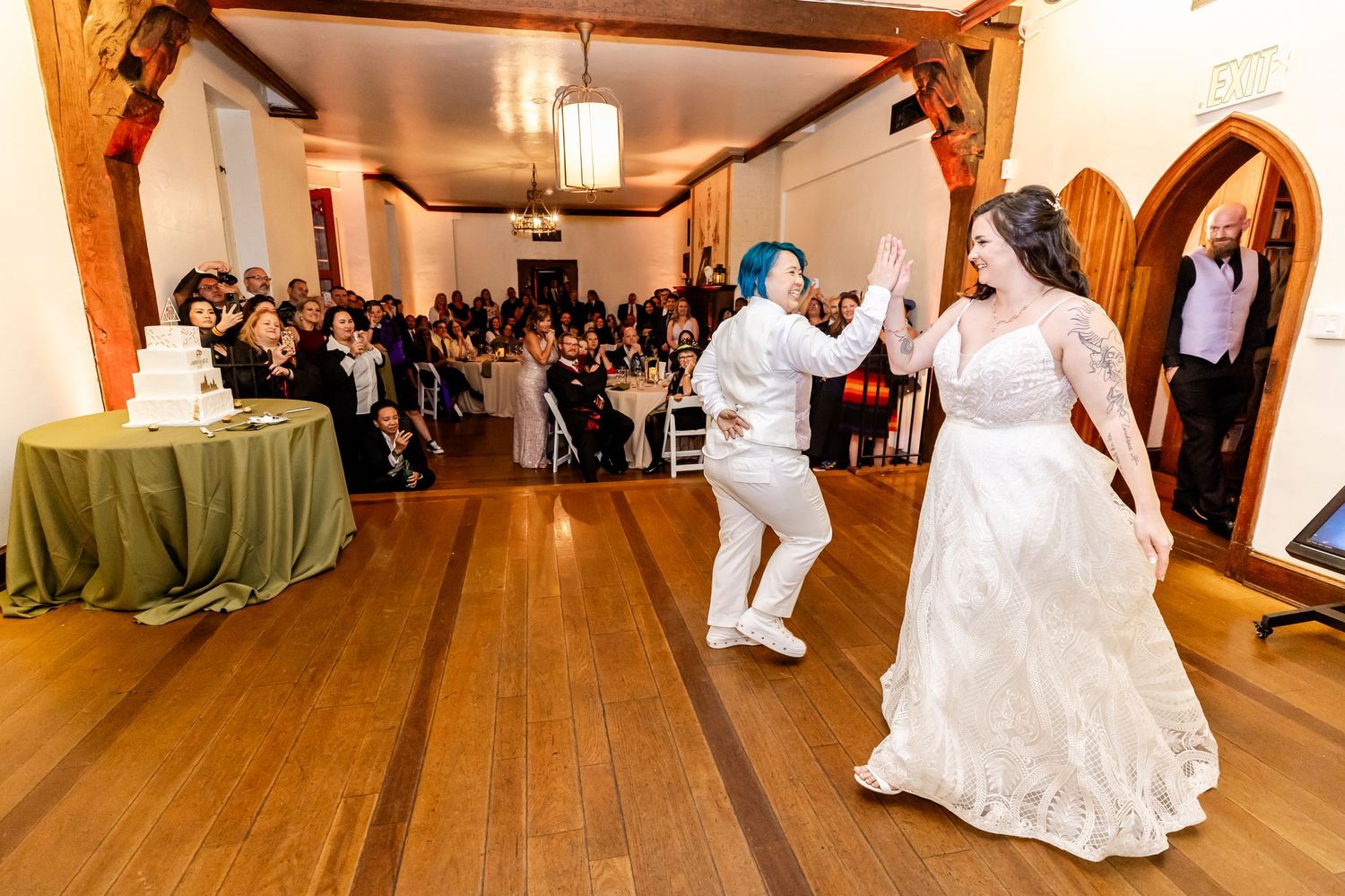 Wedding couple performing their first dance in a rustic wooden hall as guests look on.