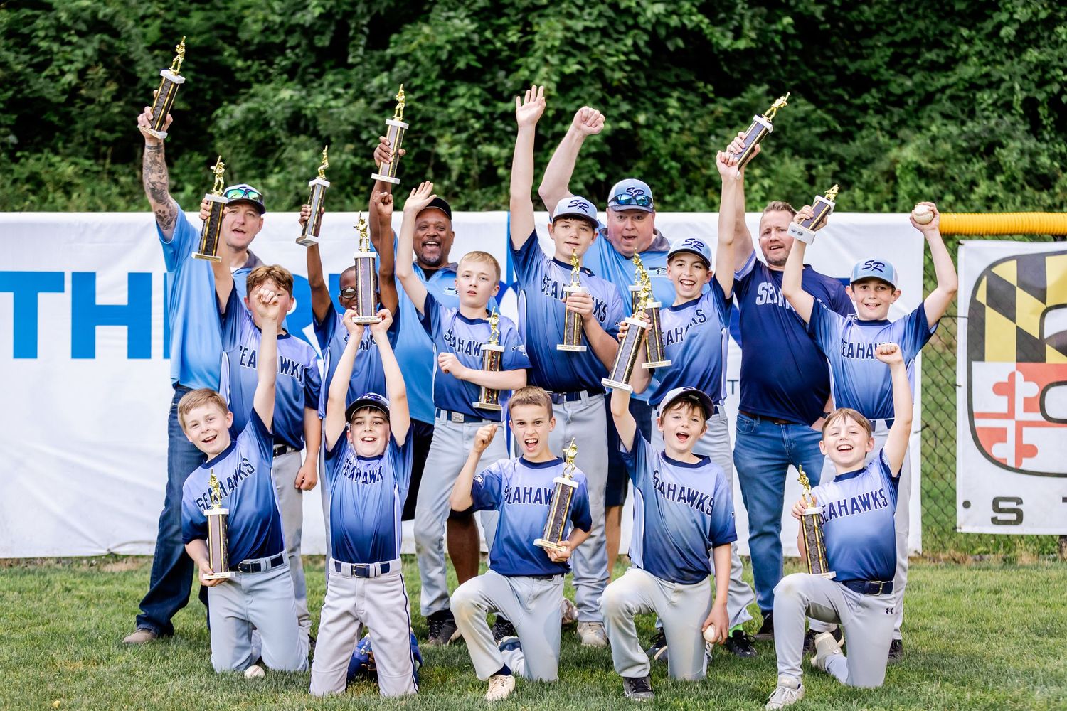 Youth baseball team in blue uniforms celebrates together on the field.