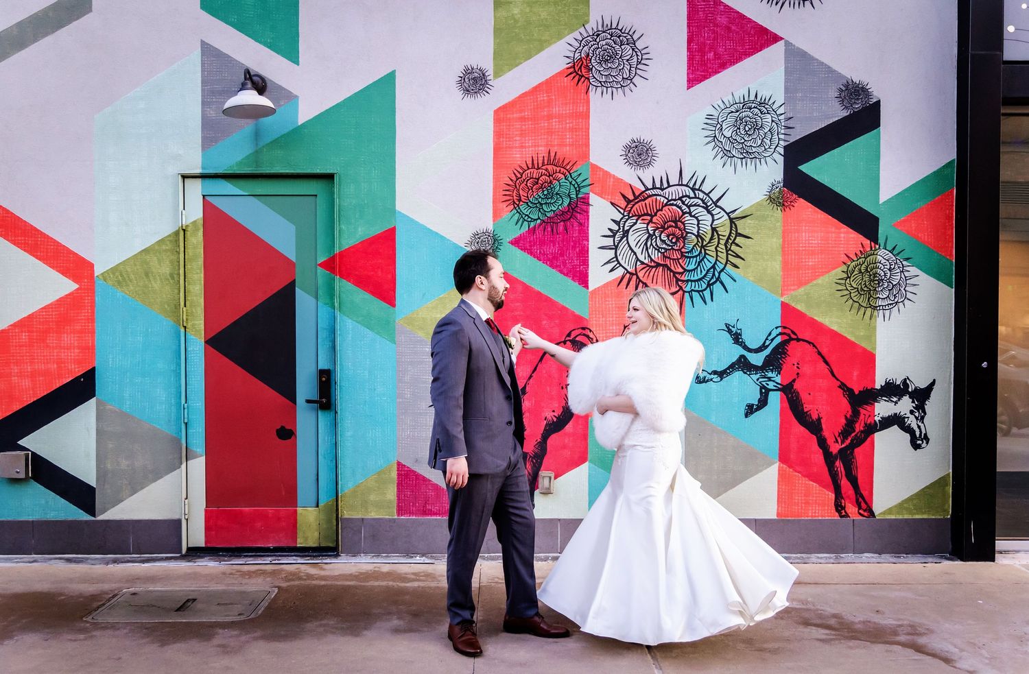 A colorful geometric mural serves as backdrop for a wedding photo shoot with figures in formal attire.