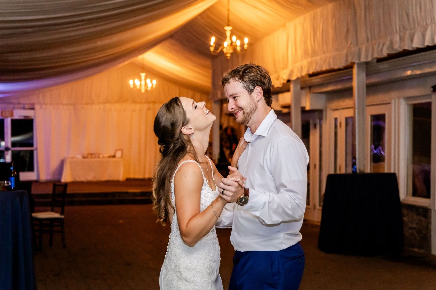 Romantic couple dancing together under warm chandelier lighting at an elegant indoor reception venue.