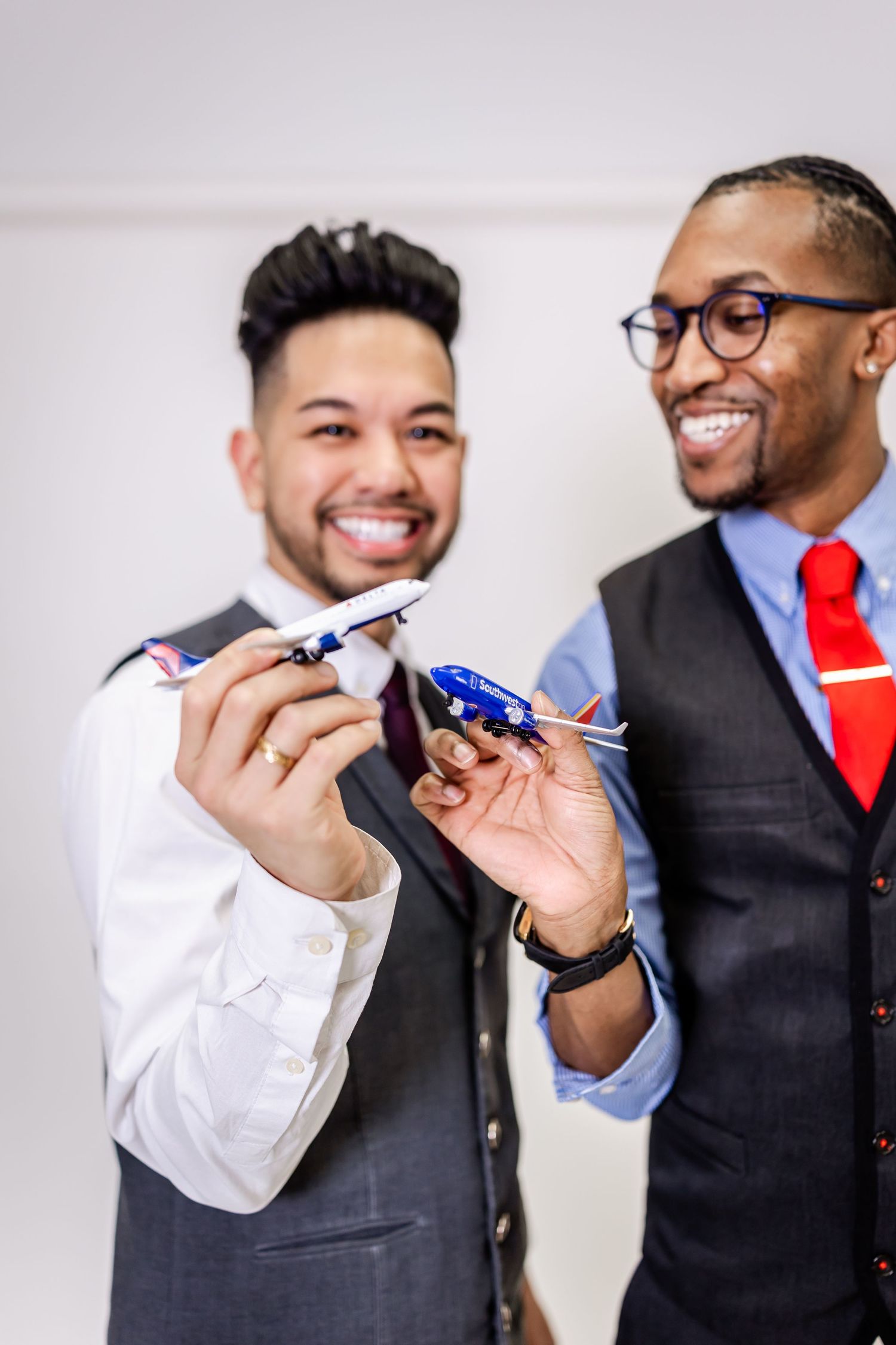 Business colleagues in vests and ties examining miniature airplanes with joyful expressions.