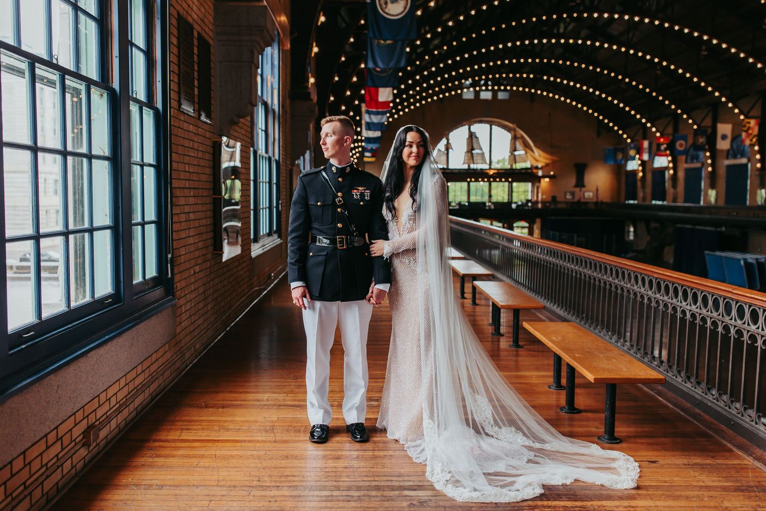 Wedding couple walks down a decorative hallway with string lights and wooden beams overhead.
