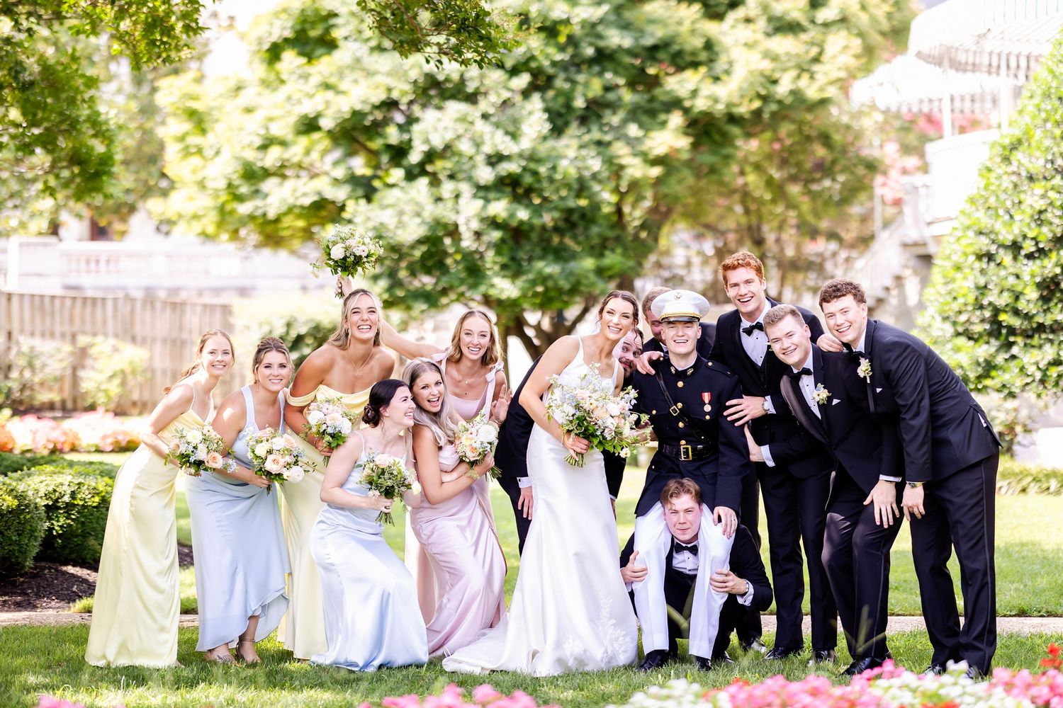 Wedding party poses outdoors in a garden setting with pink and white color scheme.