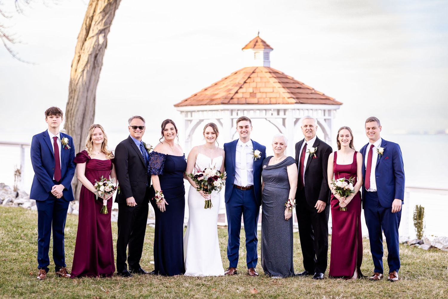 Wedding party poses together on boardwalk wearing burgundy and navy formal attire.