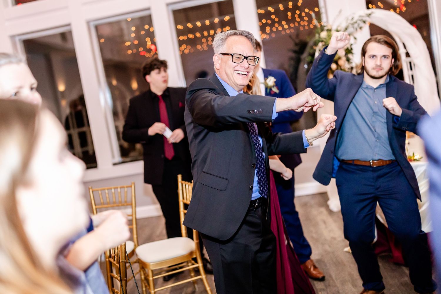 Wedding guests dancing enthusiastically under string lights at an indoor reception.