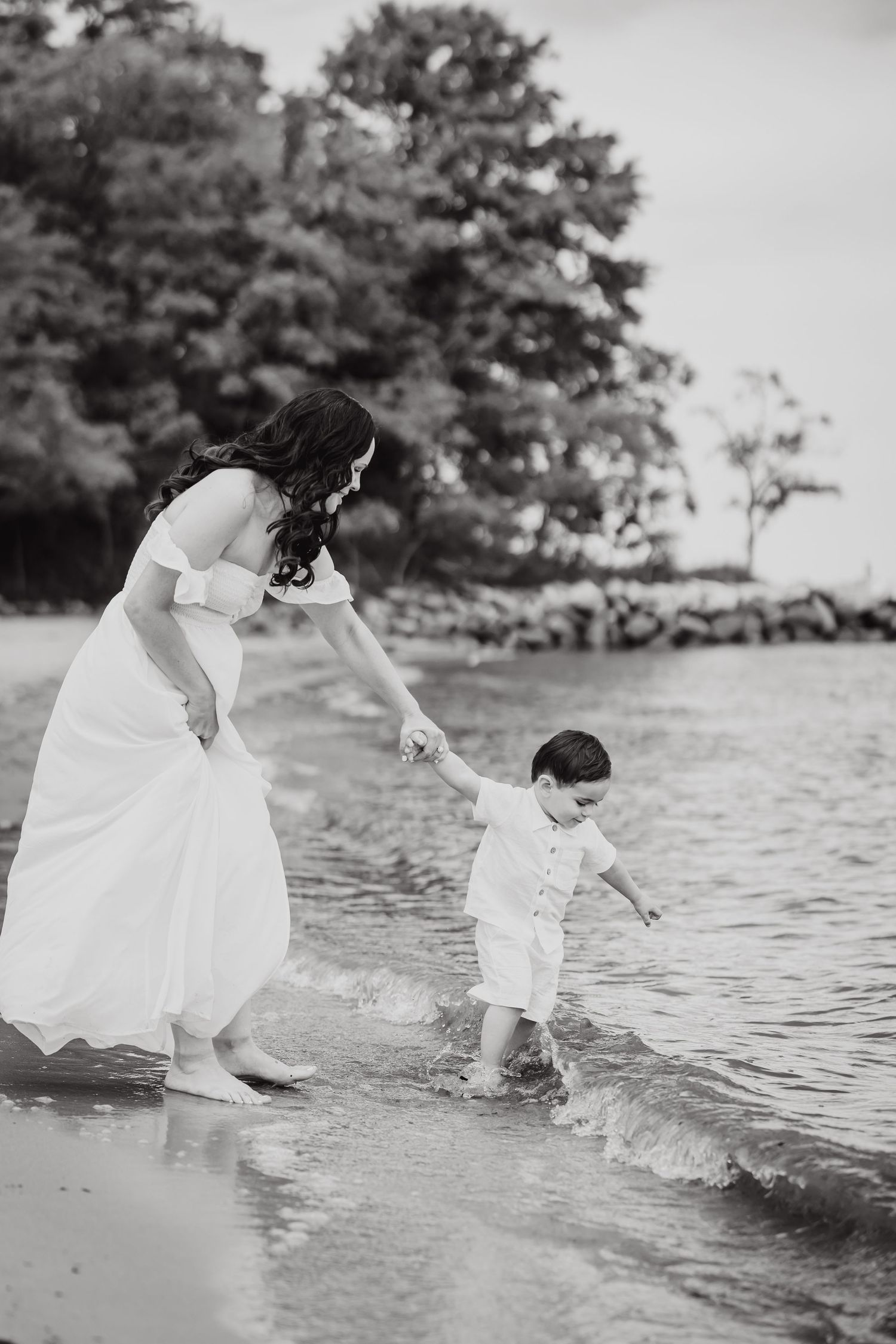 Black and white photo of woman and child playing in ocean waves at beach.