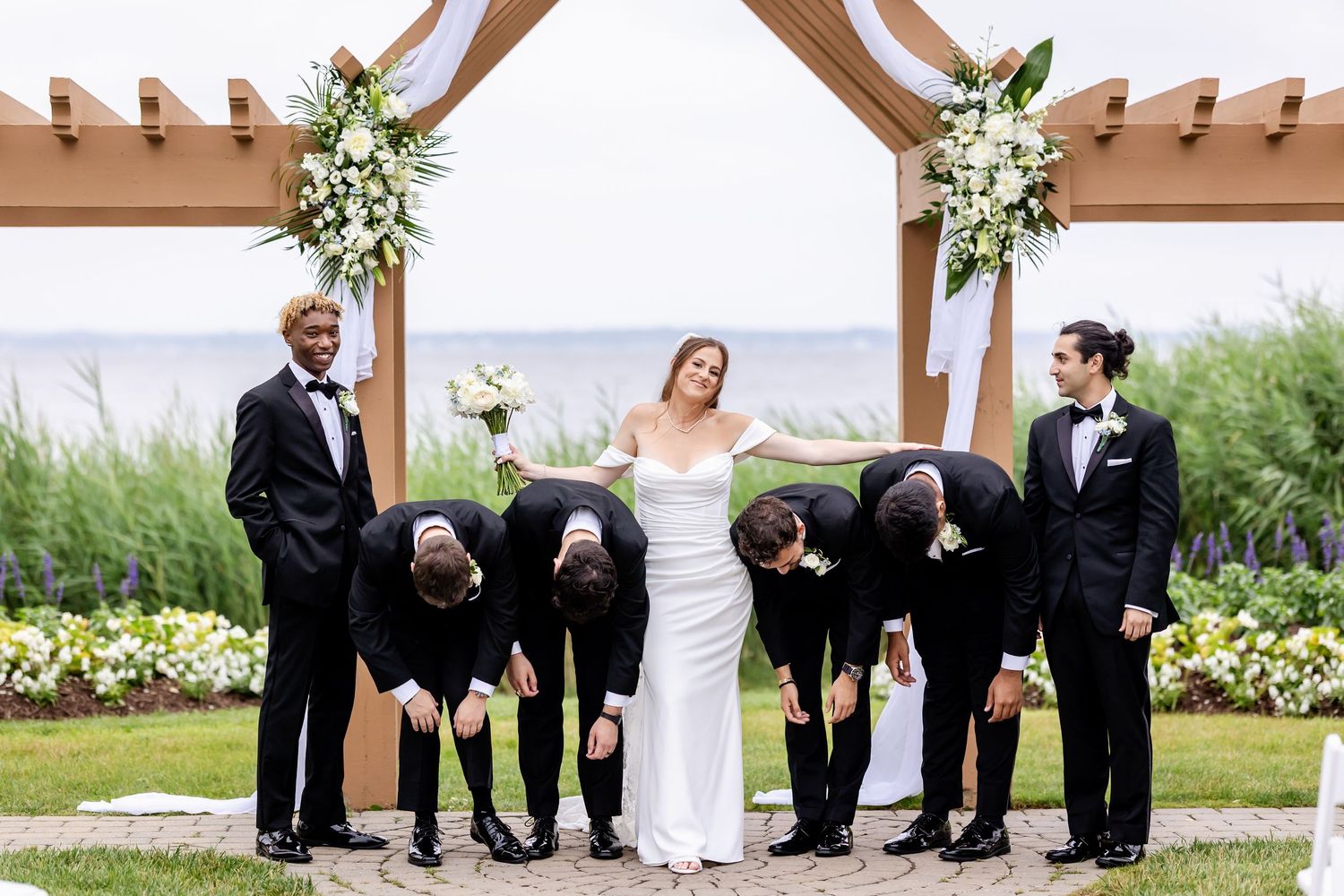 Wedding ceremony setup under a wooden pergola with white floral arrangements.