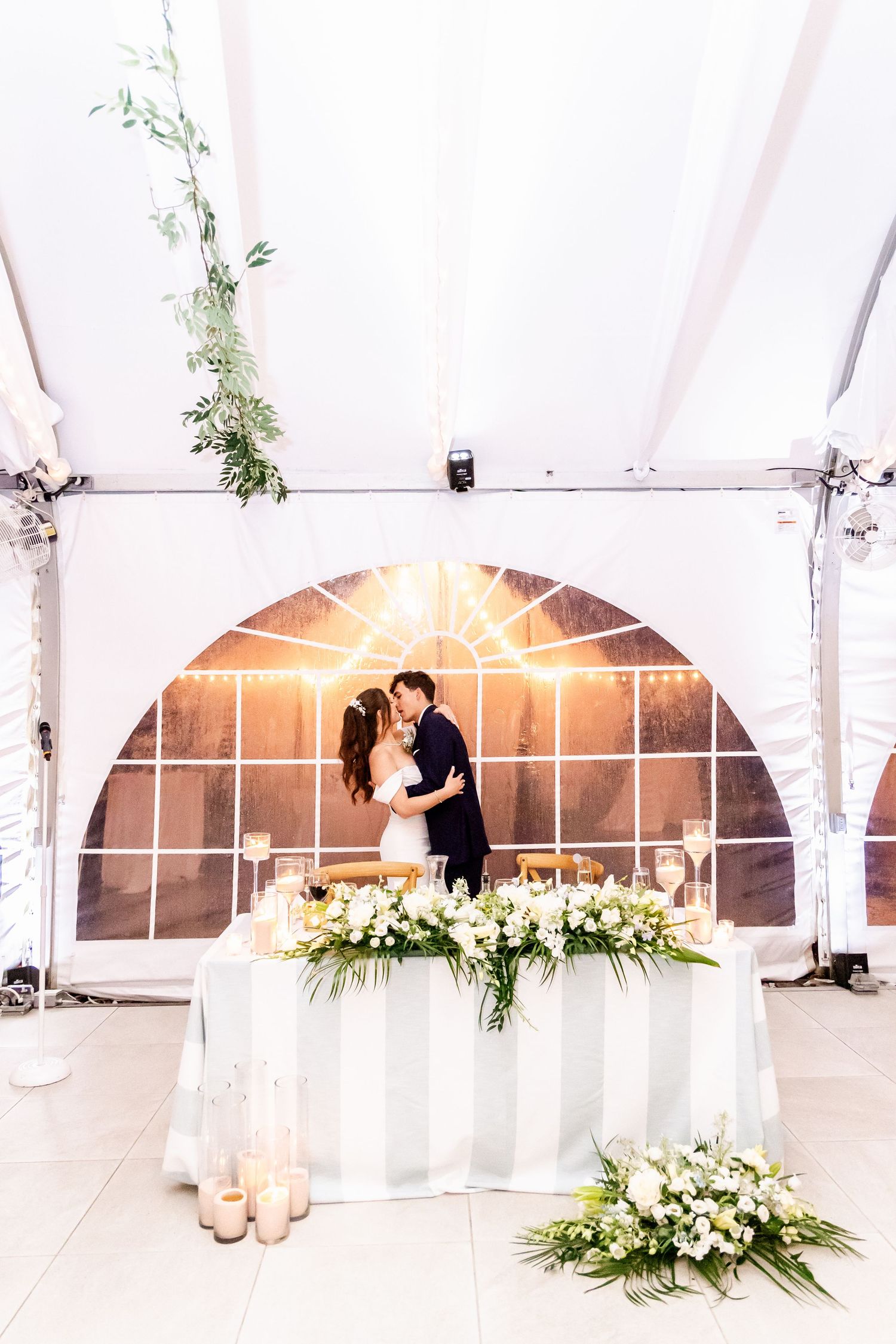 Elegant white tent wedding reception setup with floral decorations and draped fabric.