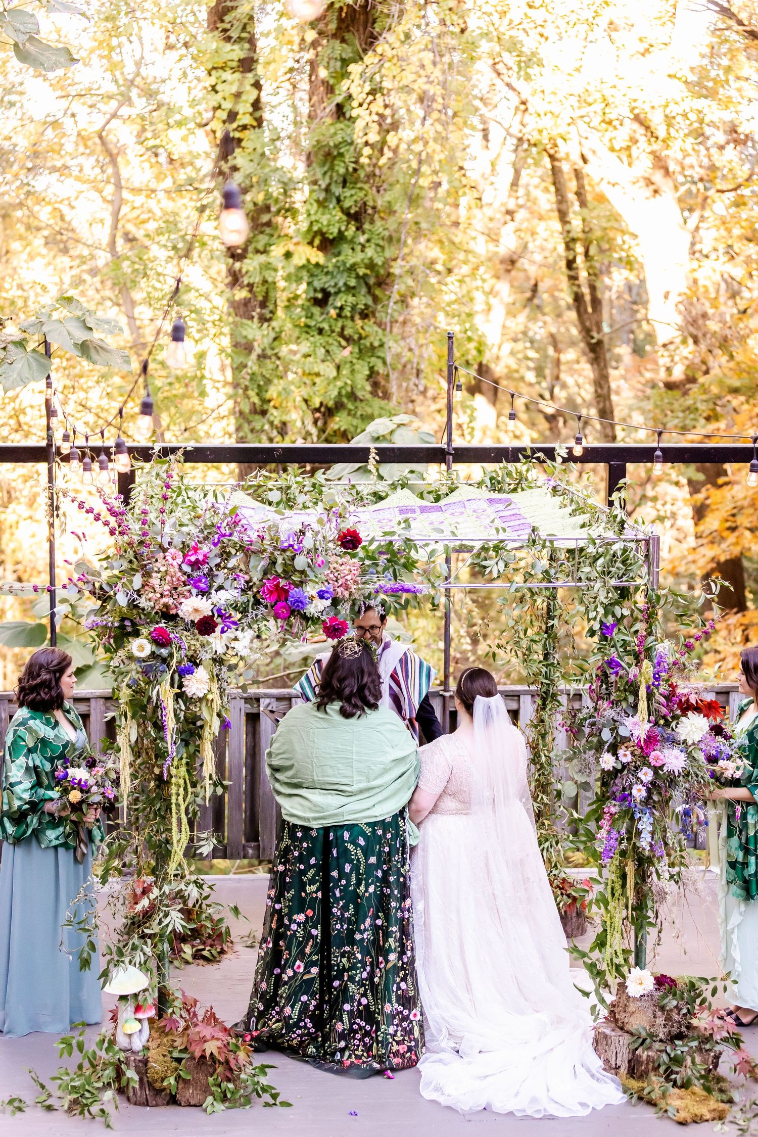 Beautiful outdoor wedding ceremony setup with purple floral arch decorations and greenery in an autumn forest setting.