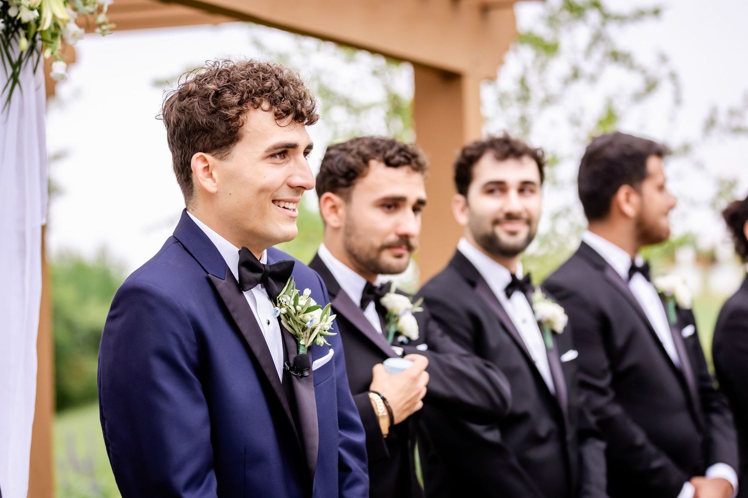 Groomsmen in navy suits stand together in formal wedding party lineup.