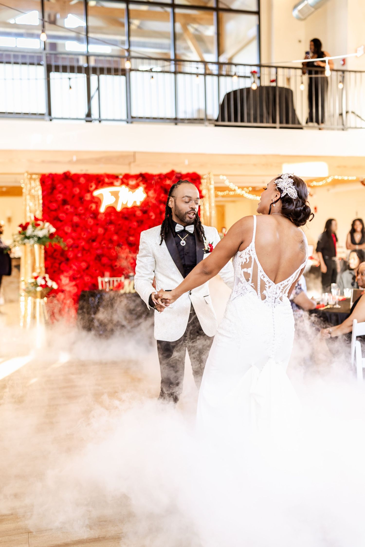 A romantic first dance at a wedding with fog effects and a stunning red rose wall backdrop in an elegant venue.