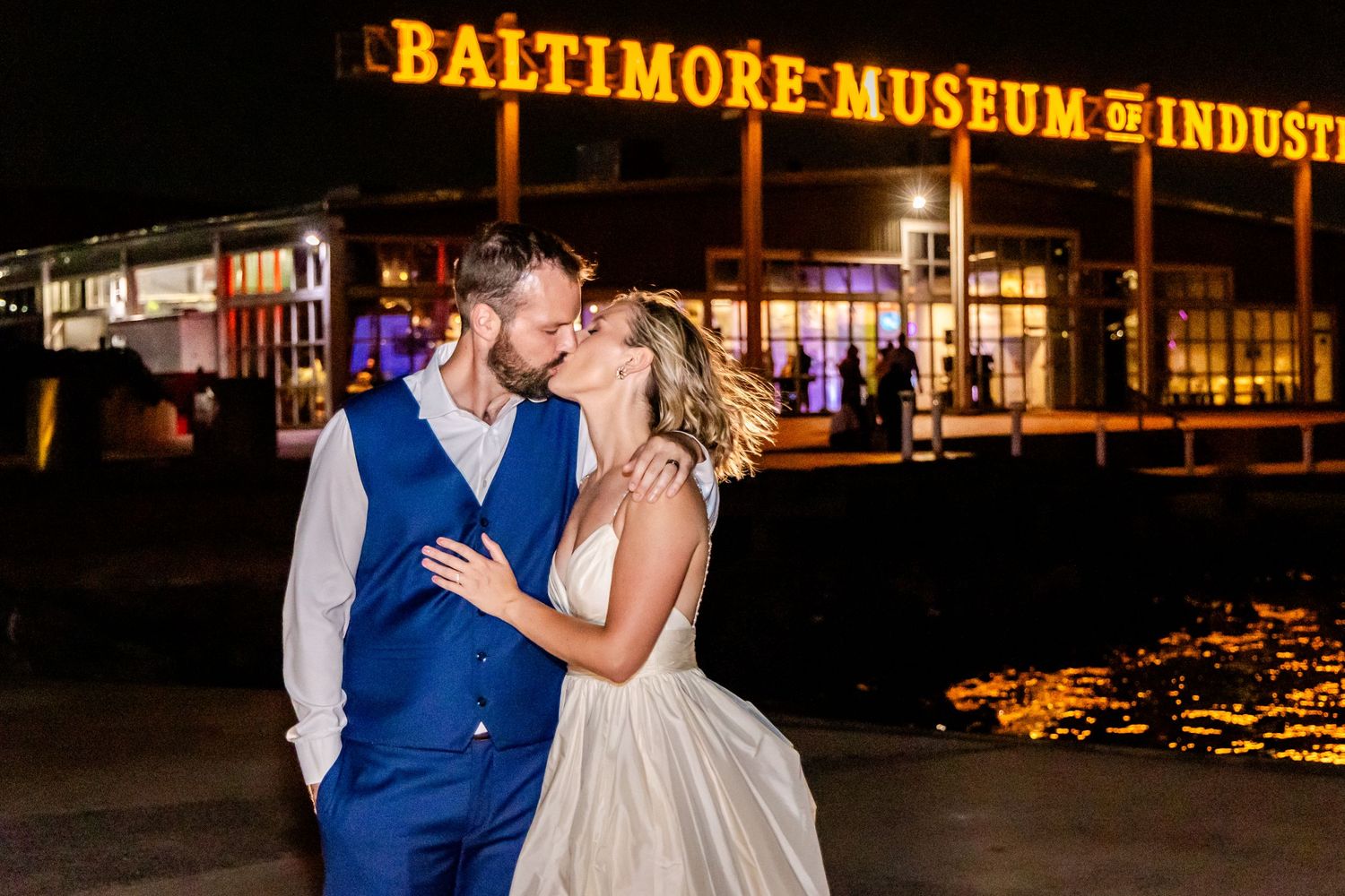 A couple shares a romantic moment at night outside the illuminated Baltimore Museum of Industry.