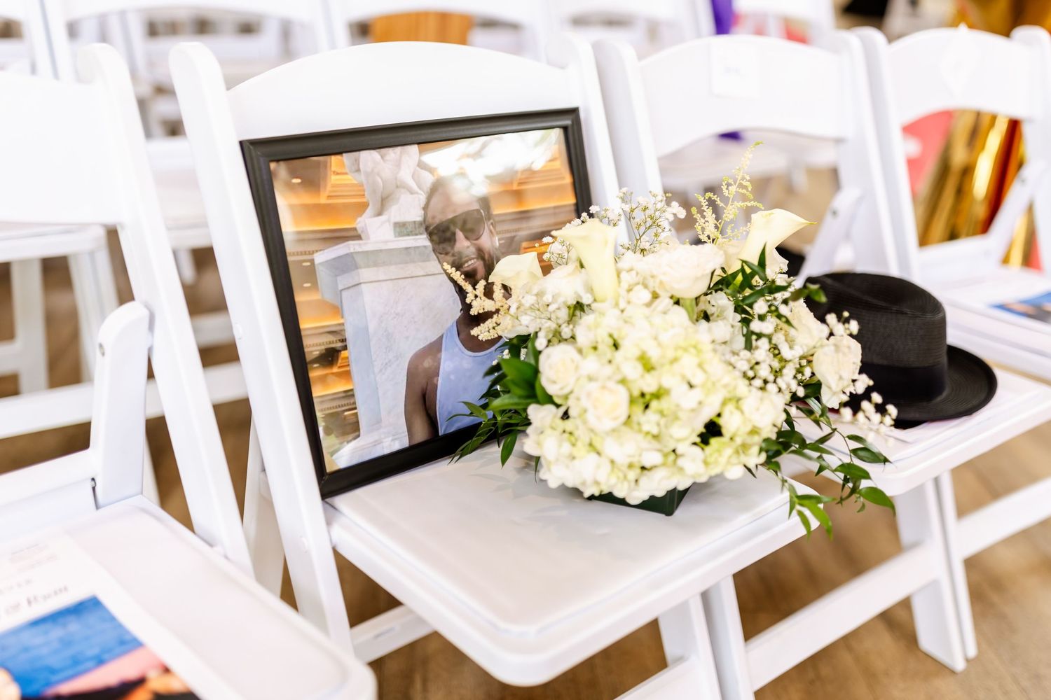 White hydrangea bouquet and framed photo displayed on white folding chair at wedding ceremony.