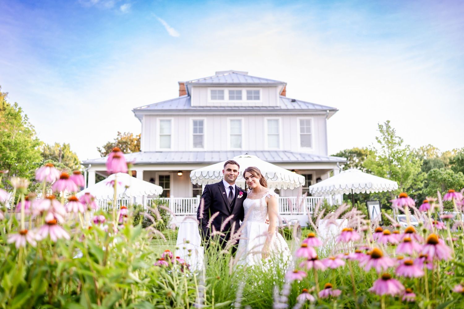 Elegant white house with pink flowers in foreground and couple in formal attire.