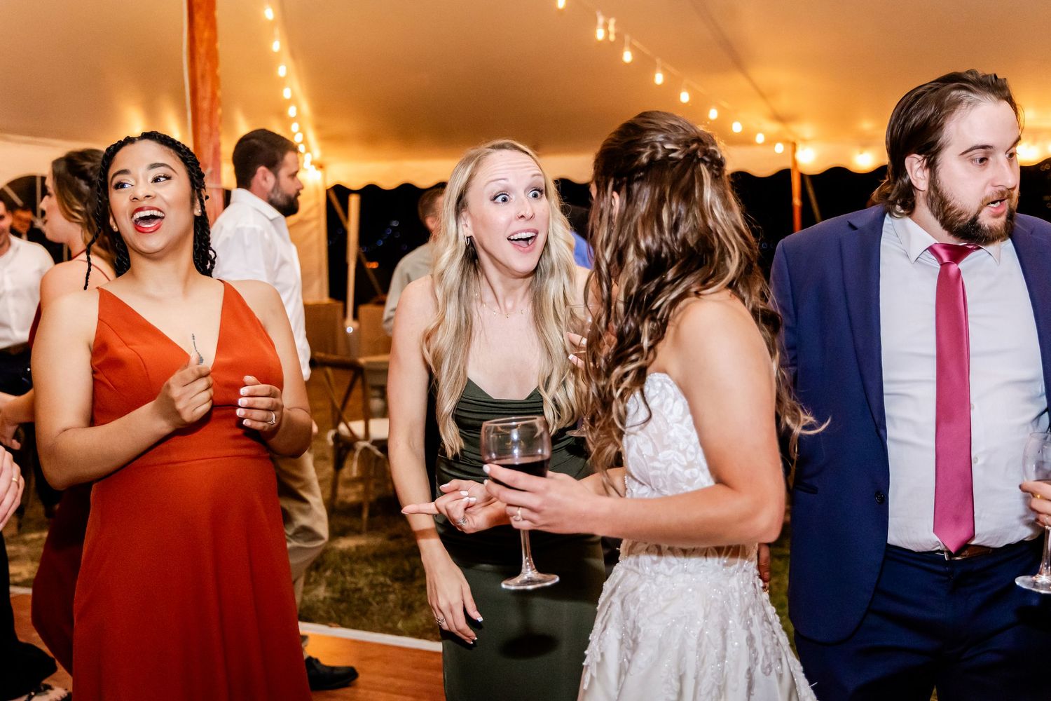 Wedding guests dancing and celebrating during reception party under warm tent lighting.