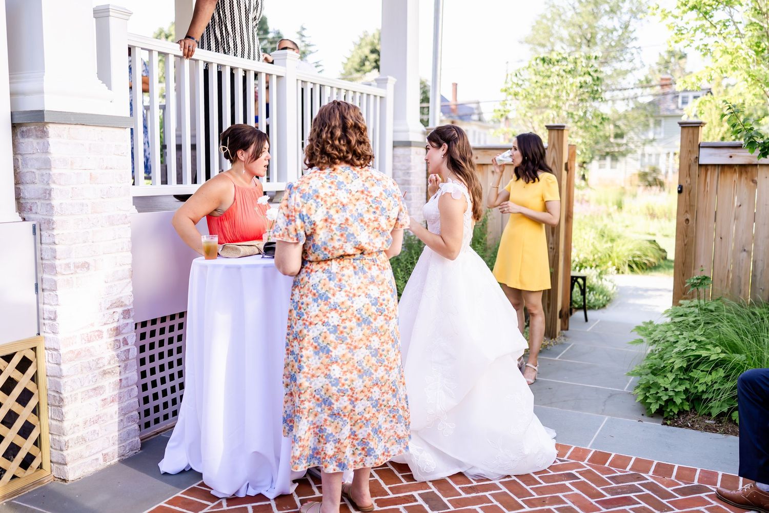 Wedding guests gathering on a white columned porch with brick foundation during a summer celebration.