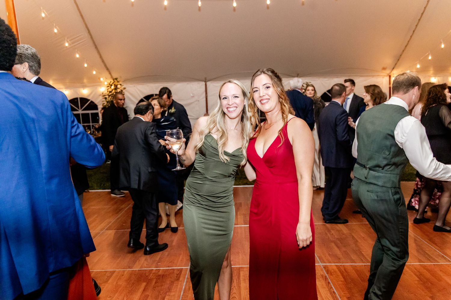Wedding guests dancing and celebrating on a wooden dance floor under a tent.